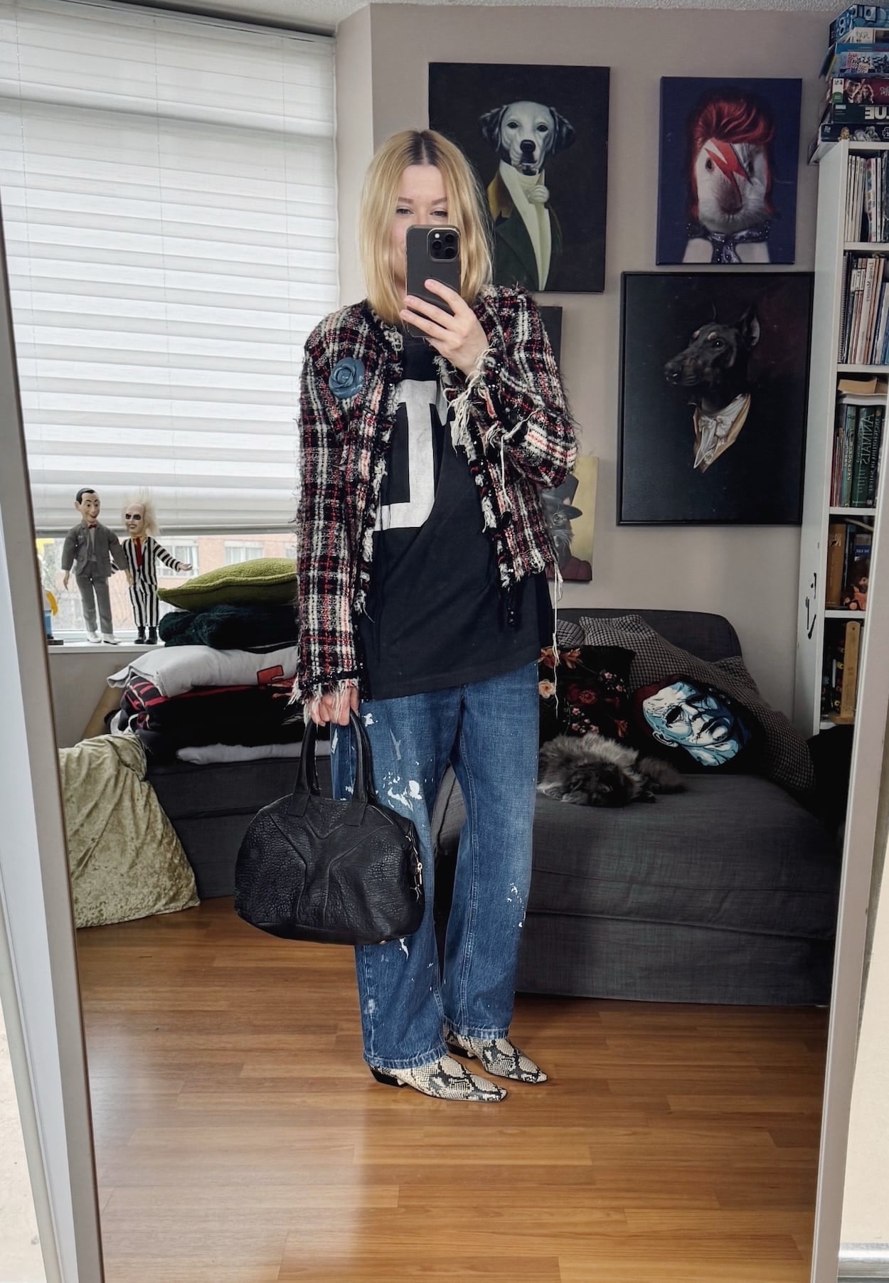 Sara of livelovesara is standing in front of a mirror taking a photo of her outfit. She is wearing an FU t-shirt under a tweed jacket, a blue flower brooch, paint splatter jeans, snake print boots, and a YSL Easy bag.