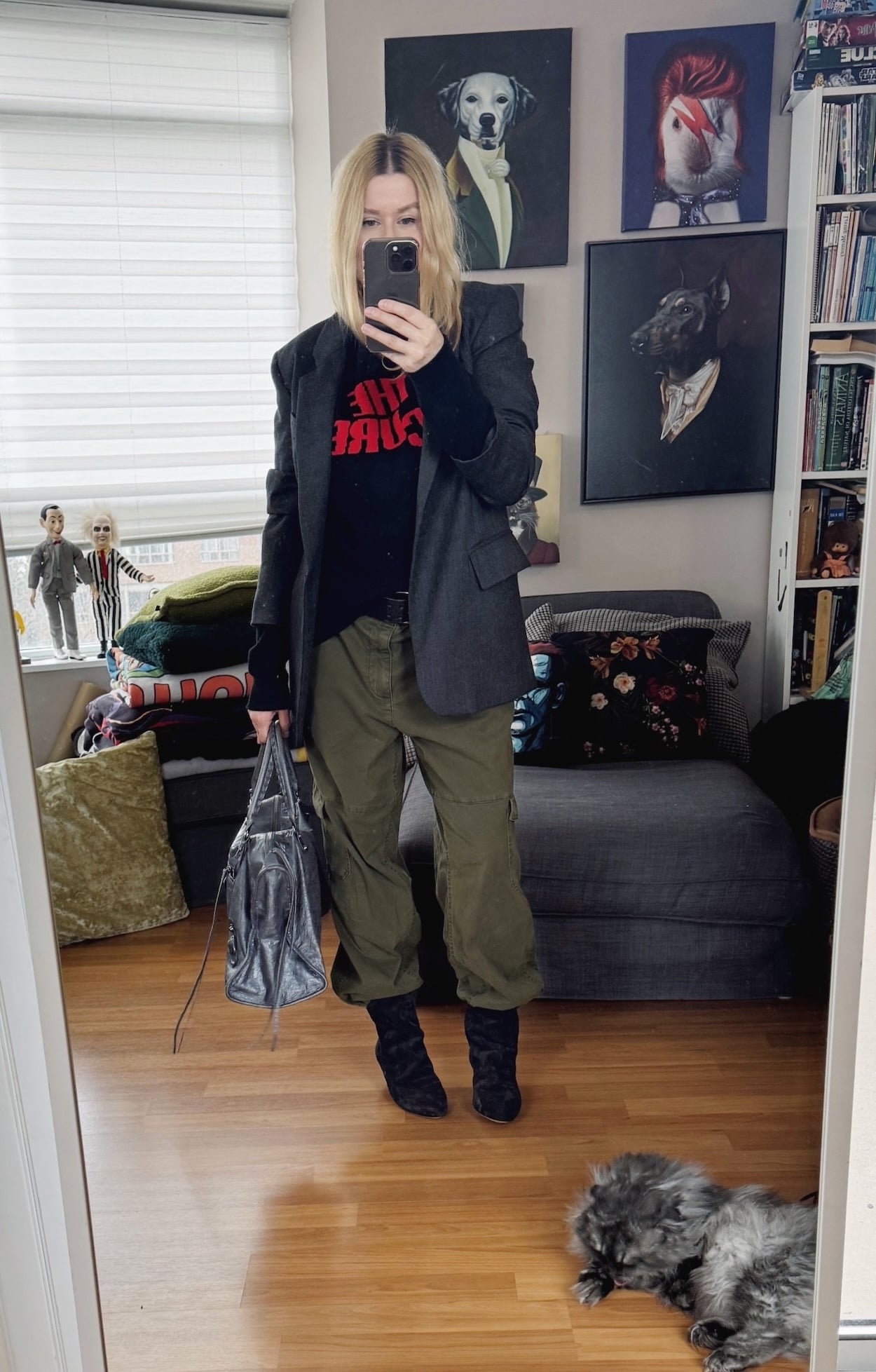 Sara of livelovesara is standing in front of a mirror taking a photo of her outfit. She is wearing a Hades Wool The Cure sweater, cargo pants with a studded belt, a grey blazer, slouchy black boots, and a grey Balenciaga work bag.