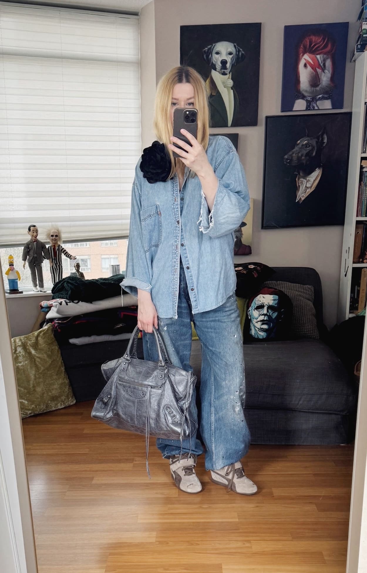 Sara of livelovesara is standing in front of a mirror taking a photo of her outfit. She is wearing a vintage Levi's denim shirt with a large black flower brooch, paint splattered jeans, brown wedge sneakers, and a grey Balenciaga work bag.