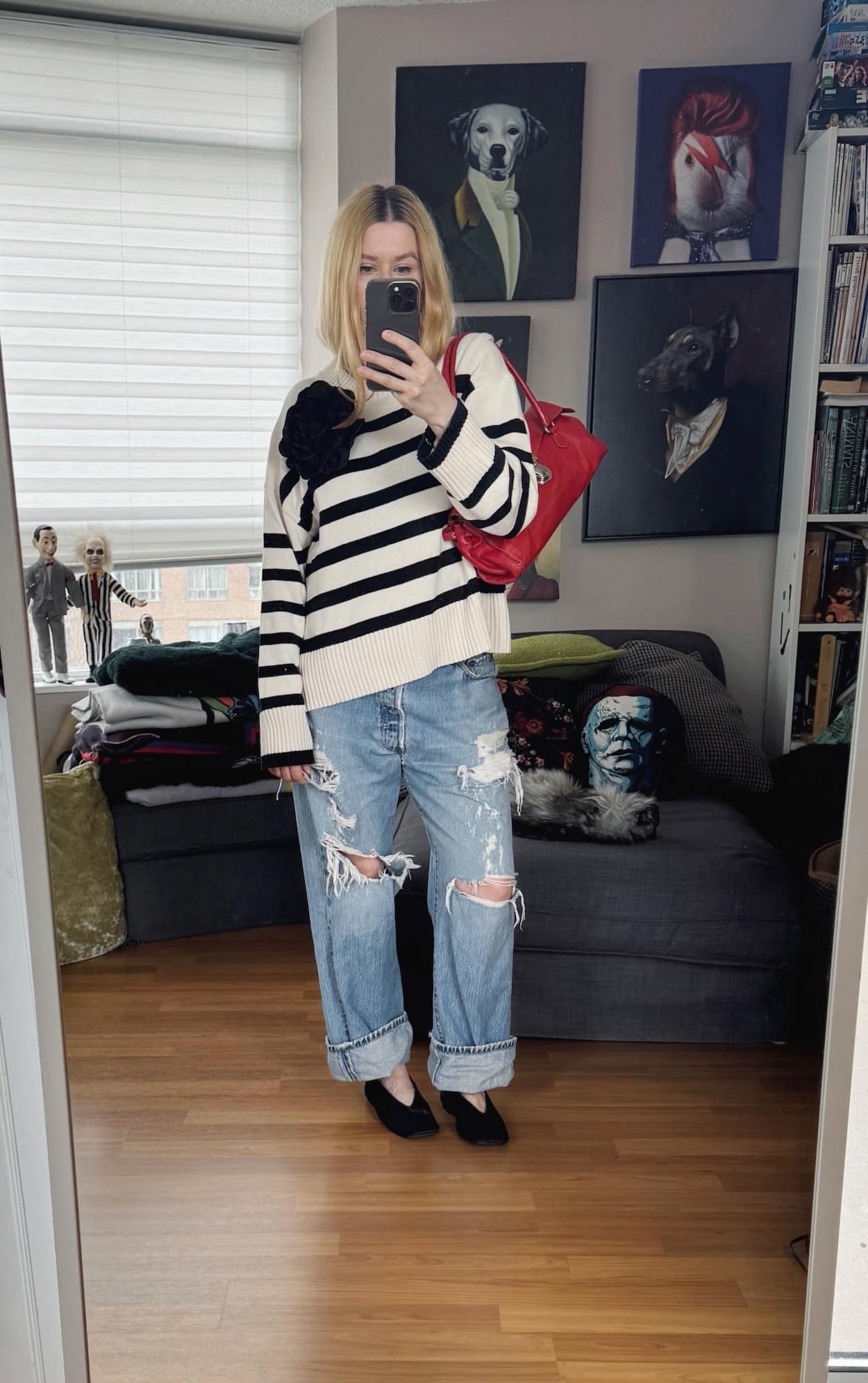 Sara of livelovesara is standing in front of a mirror taking a photo of her outfit. She is wearing a black and cream striped sweater, vintage distressed Levis, black pony hair flats, a large black flower brooch, and a red Prada bag.