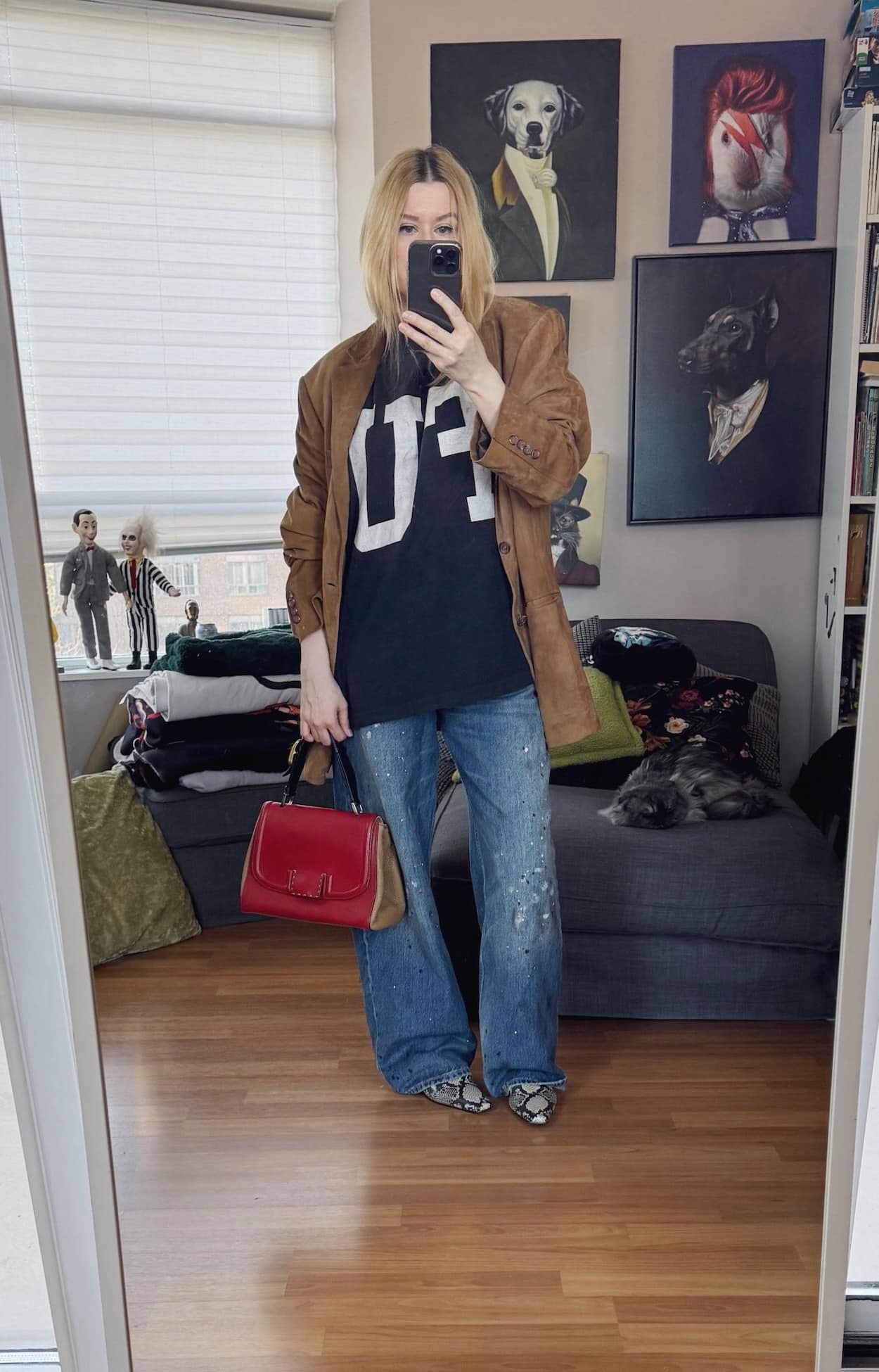 Sara of livelovesara is standing in front of a mirror taking a photo of her outfit. She is wearing a black Shirt with a Large FU letters on the front with paint splatter jeans, a mens brown suede blazer, snake print boots, and a Fendi Silvana bag.