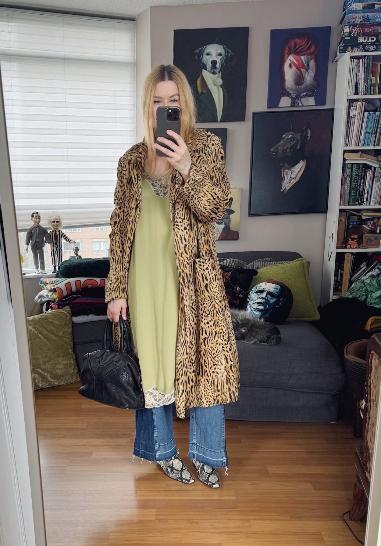 Sara of livelovesara is standing in front of a mirror taking a photo of her outfit. She is wearing a green slip dress over flared jeans, and vintage animal print jacket, snake print boots, and a black YSL easy bag.