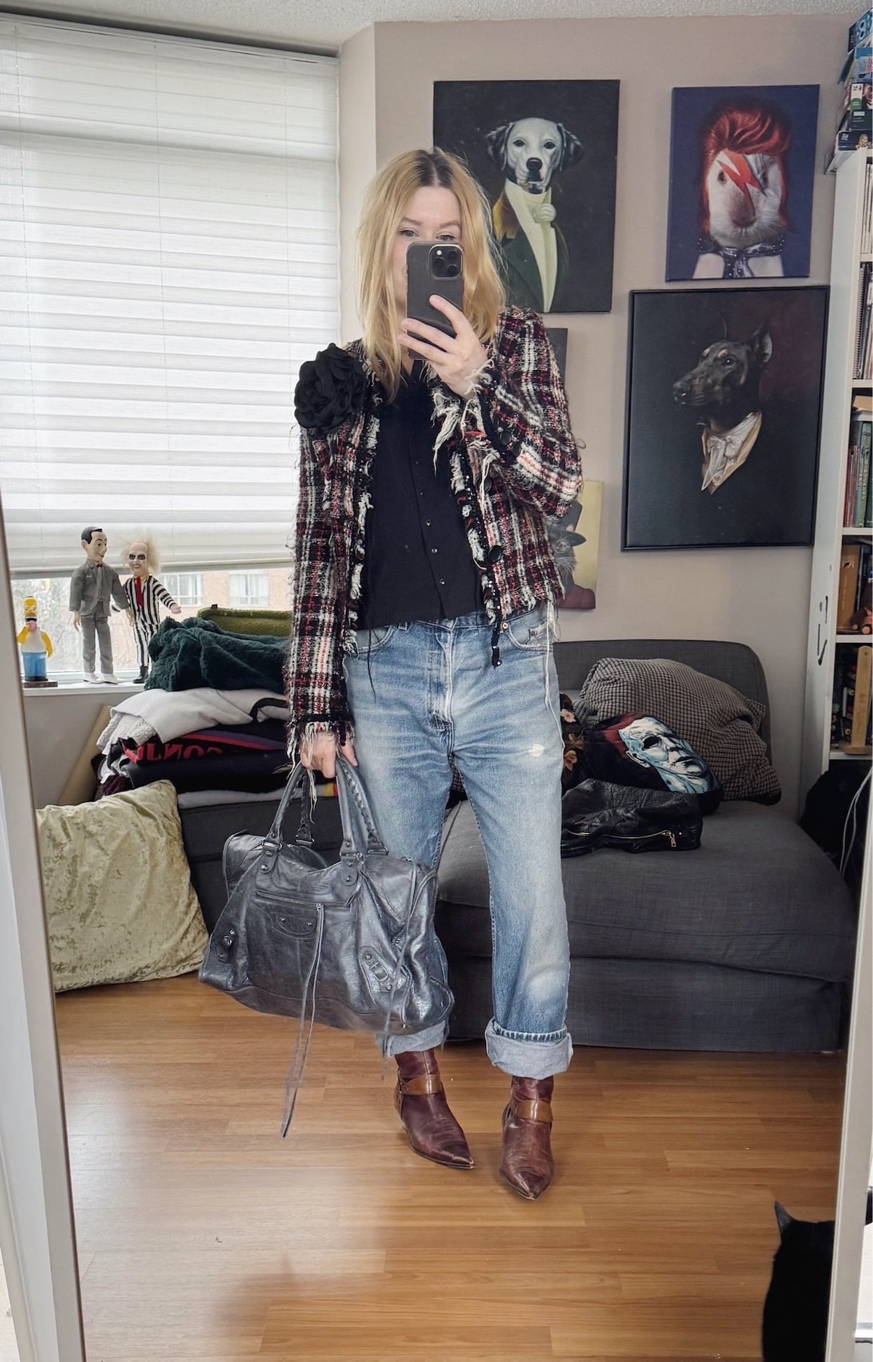 Sara of livelovesara is standing in front of a mirror taking a photo of her outfit. She is wearing an black shirt under a tweed jacket with a large black brooch, vintage Levis, 90s brown boots, and a grey Balenciaga bag.