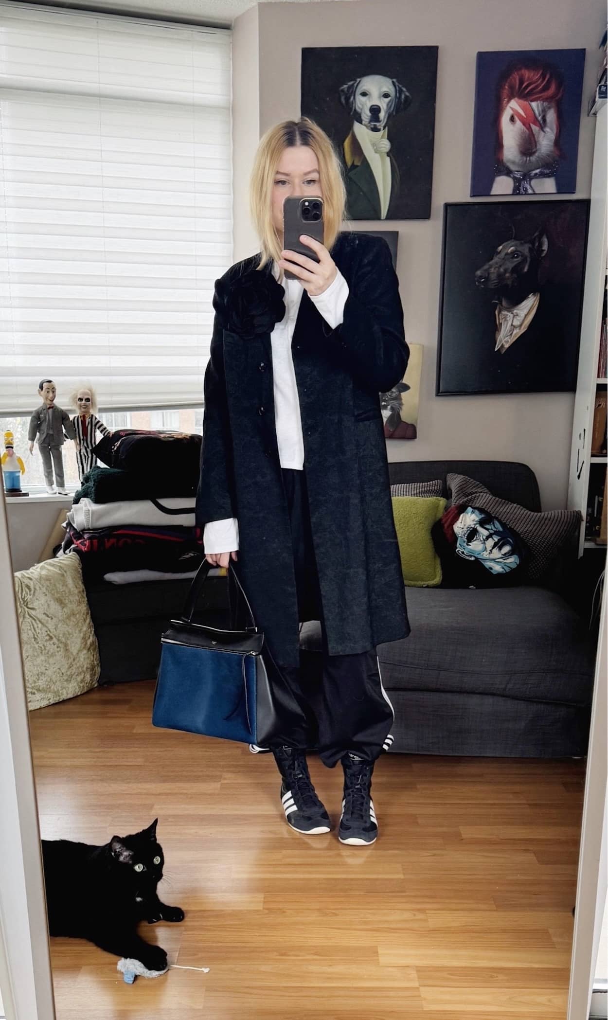 Sara of livelovesara is standing in front of a mirror taking a photo of her outfit. She is wearing awhite long sleeve under a Dries Van Noten jacket, black Adidas track pants, Adidas boxing sneakers, and a blue Celine Edge bag.