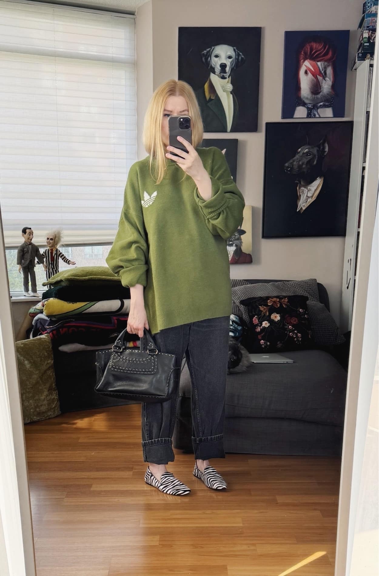 Sara of livelovesara is standing in front of a mirror taking a photo of her outfit. She is wearing an green Adidas sweater with black vintage Levis, zebra print loafers, and a celine boogie bag.