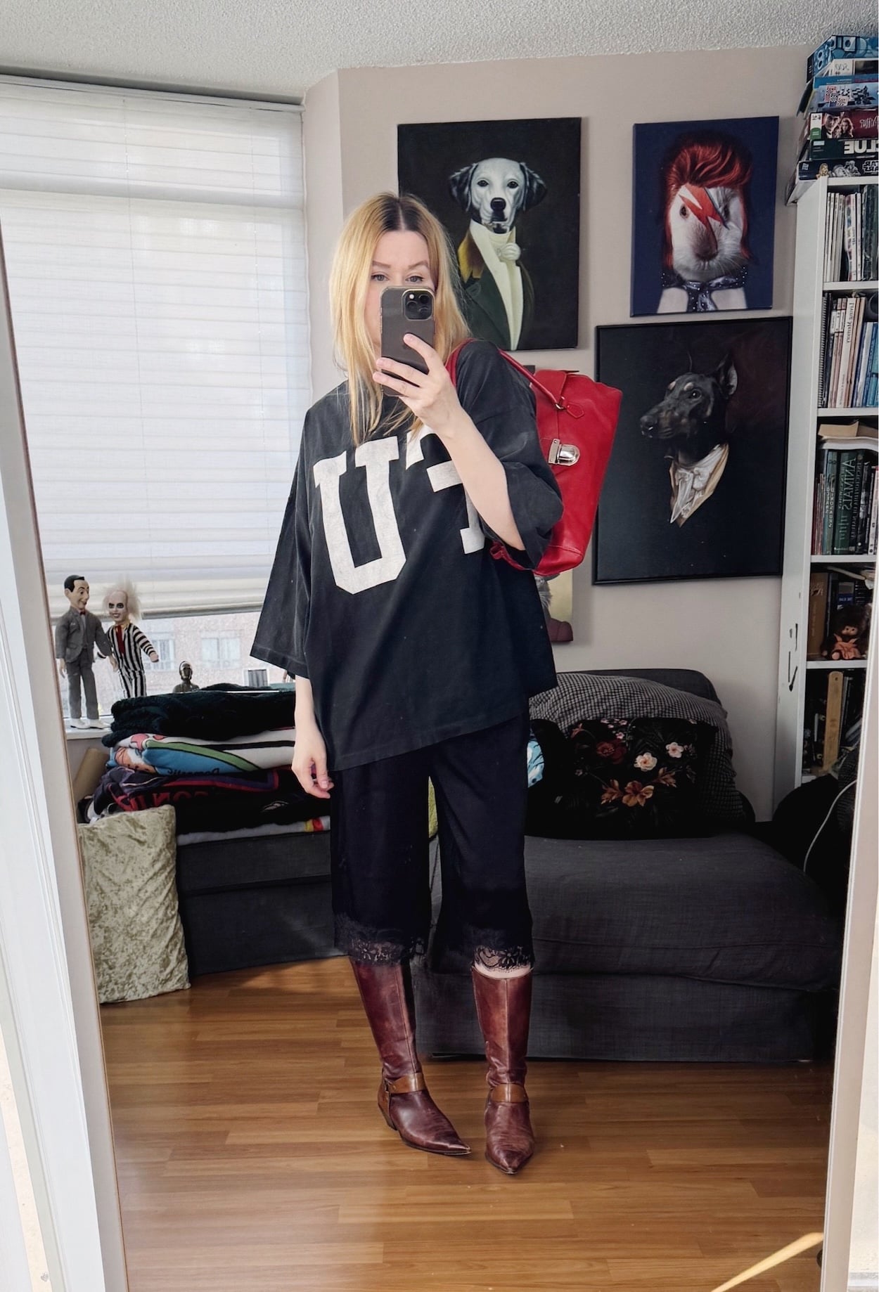 Sara of livelovesara is standing in front of a mirror taking a photo of her outfit. She is wearing a red plaid shirt with an FU Oversized shirt with silk Bermuda shorts, 90s brown knee high boots, and a Y2K Prada bag in red.