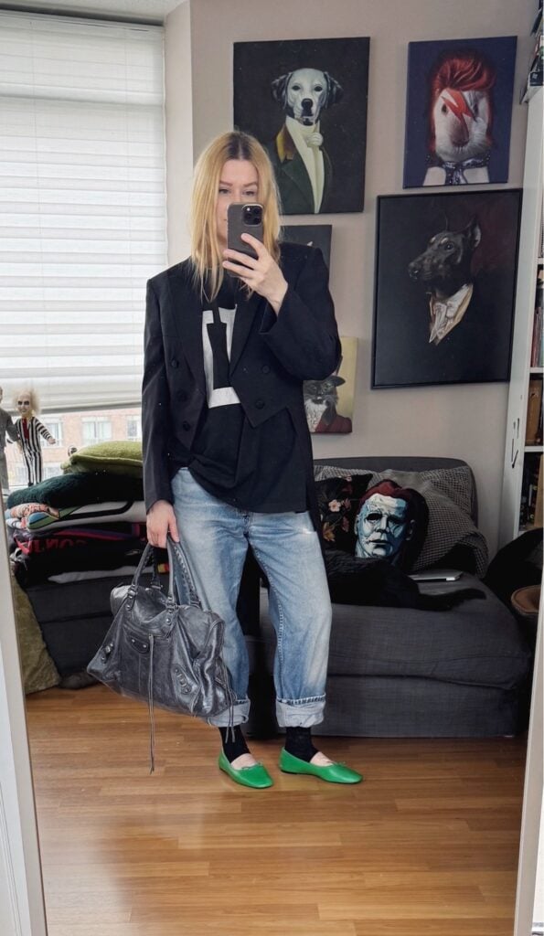 Sara of livelovesara is standing in front of a mirror taking a photo of her outfit. She is wearing an FU t-shirt under a vintage tailcoat, vintage Levis, green ballet flats, and a grey Balenciaga bag.