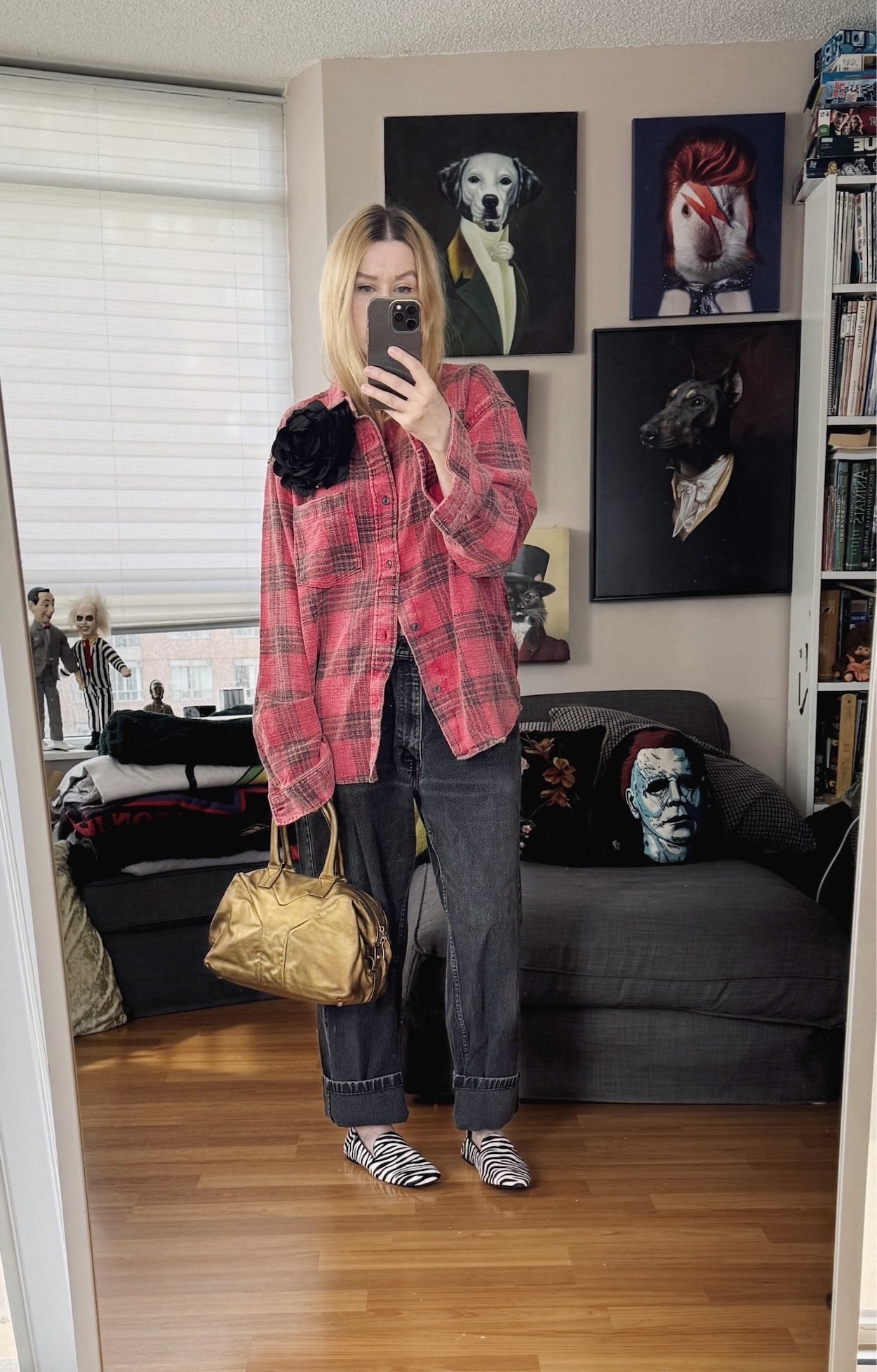Sara of livelovesara is standing in front of a mirror taking a photo of her outfit. She is wearing a red plaid shirt with a black flower brooch, black vintage levis, zebra print loafers, and a gold ysl easy bag.