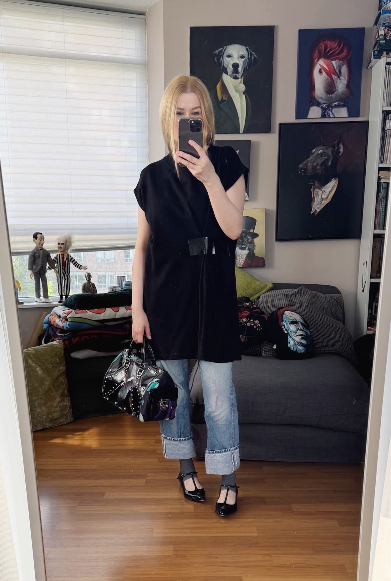 Sara of livelovesara is standing in front of a mirror taking a photo of her outfit. She is wearing an Margiela tape accent tunic with vintage levis, half socks, black t-strap mary janes, and a Y2K Versace bag.