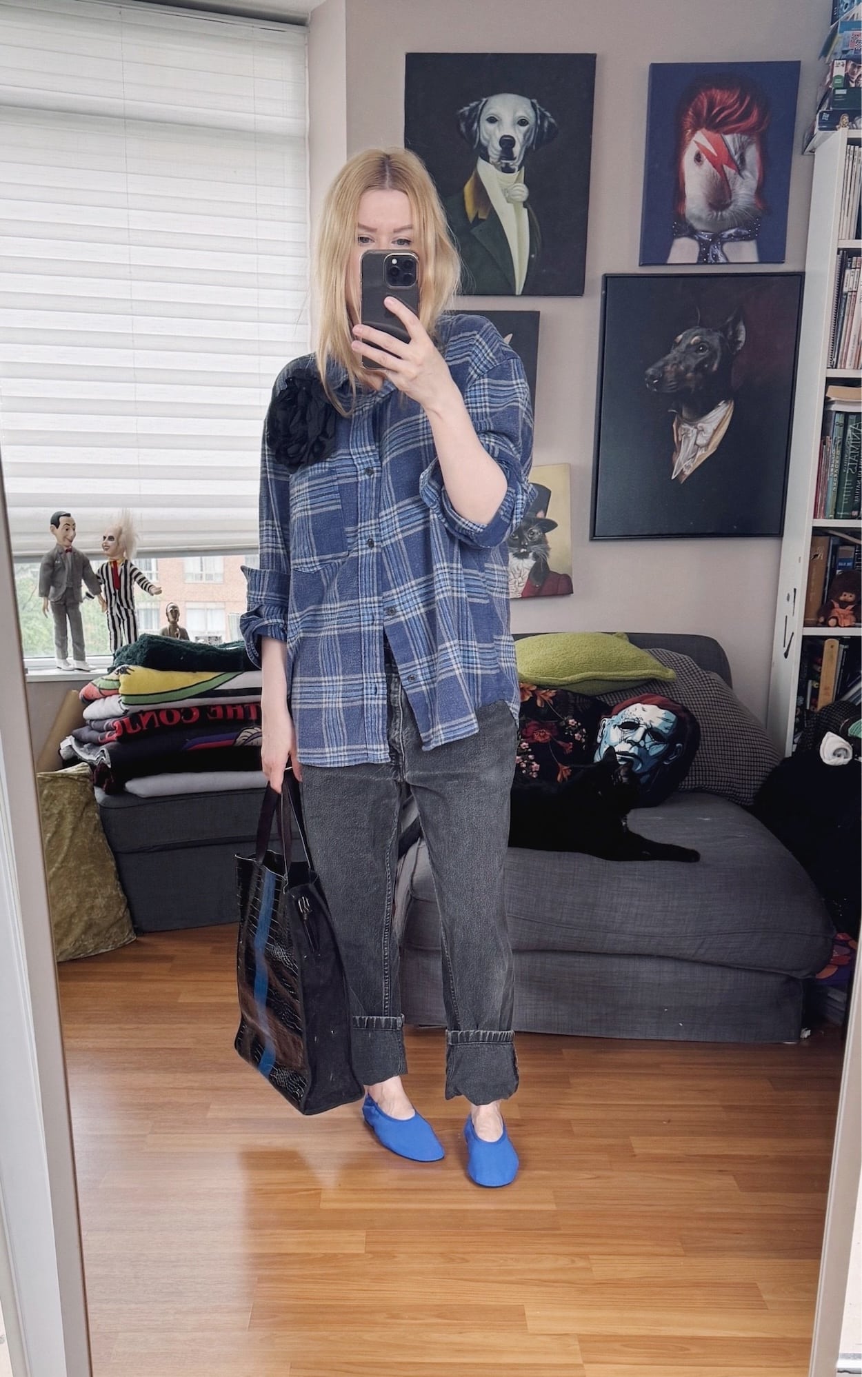 Sara of livelovesara is standing in front of a mirror taking a photo of her outfit. She is wearing a blue plaid shirt with a black flower brooch, grey-black vintage Levi's, blue ballet flats, and a black and blue striped tote.