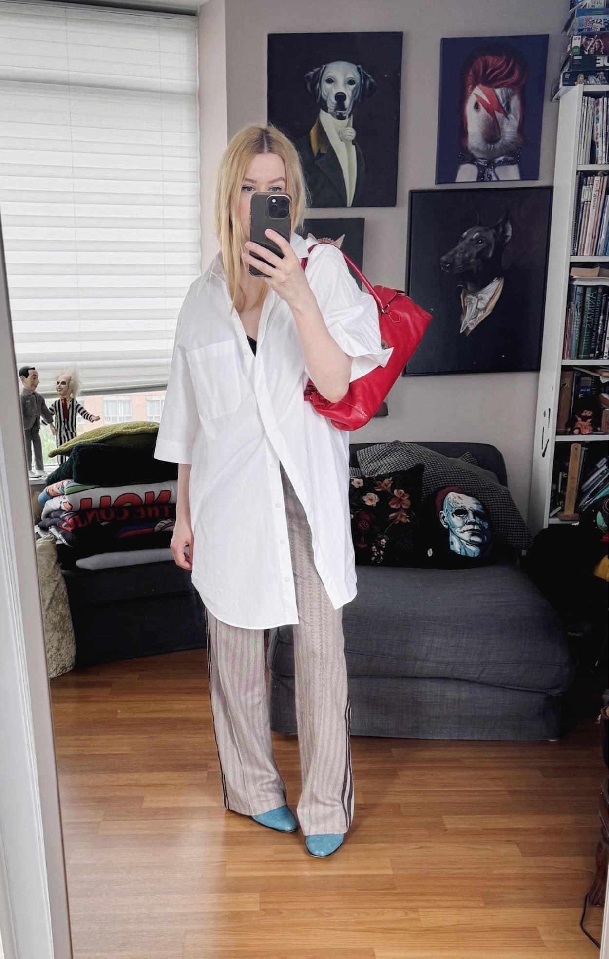 Sara of livelovesara is standing in front of a mirror taking a photo of her outfit. She is wearing an oversized, short sleeve, white buton up over houndstooth track pants, blue derby shoes, and is carrying a vintage, red Prada bag.