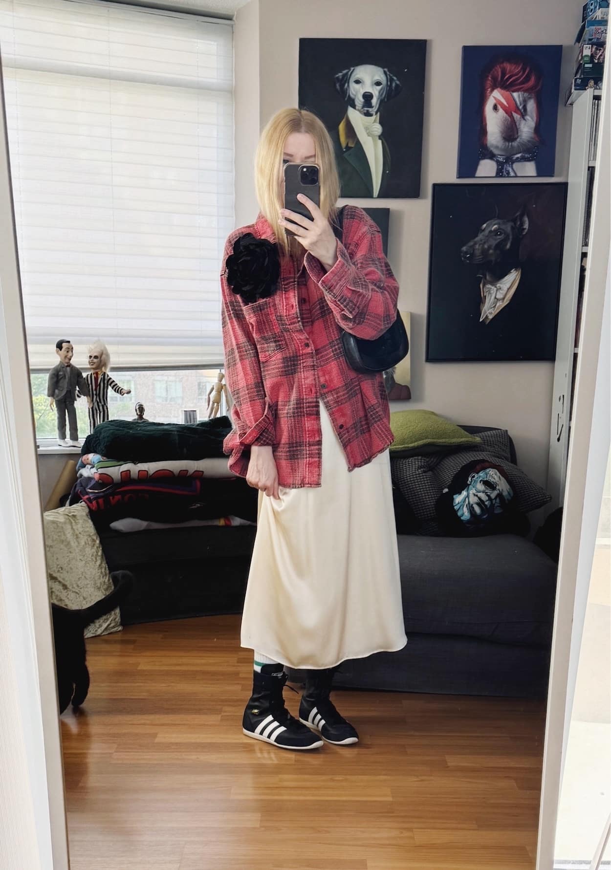 Sara of livelovesara is standing in front of a mirror taking a photo of her outfit. She is wearing a red plaid shirt over a cream slip dress, black Adidas wrestling sneakers, a black flower brooch, and a black vintage flower brooch.