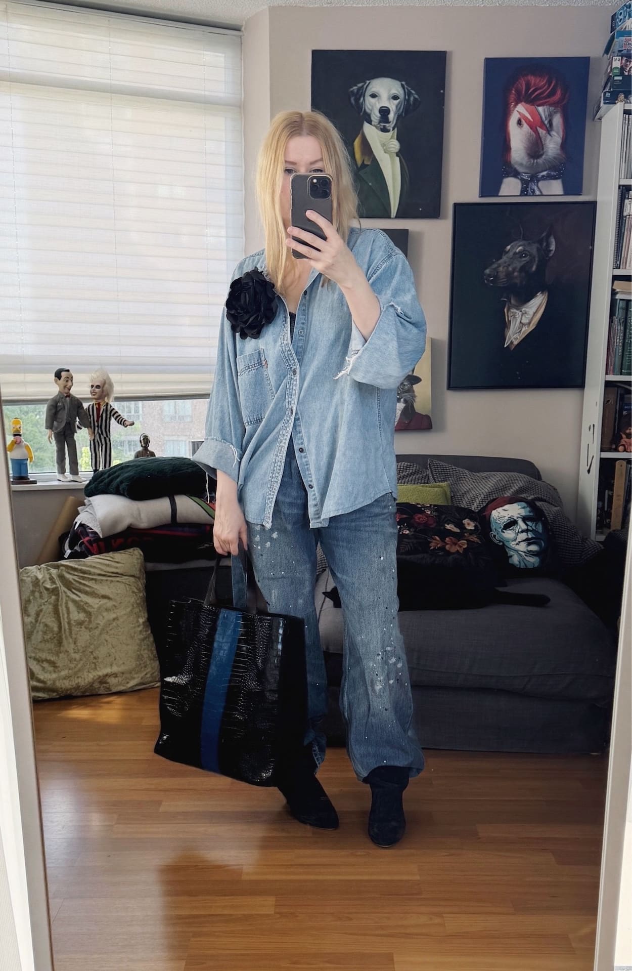 Sara of livelovesara is standing in front of a mirror taking a photo of her outfit. She is wearing a vintage levi's denim shirt, denim splattered jeans, black slouchy boots, a black flower brooch, and a striped tote bag.