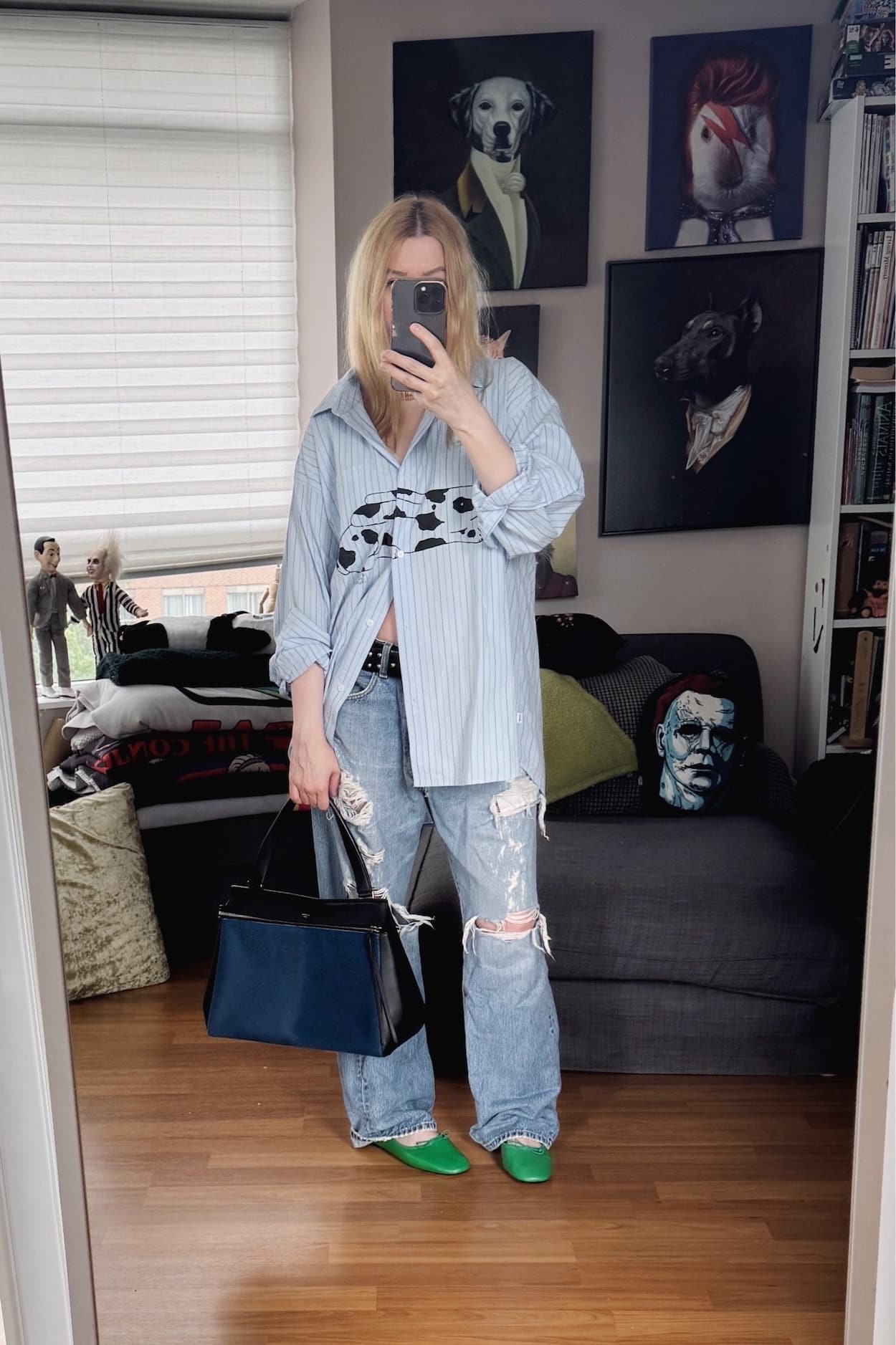 Sara of livelovesara is standing in front of a mirror taking a photo of her outfit. She is wearing a blue striped button up with a rabbit drawn on front, destressed vintage levis, green ballet flats, and is carrying a blue pony hair Celine edge bag.