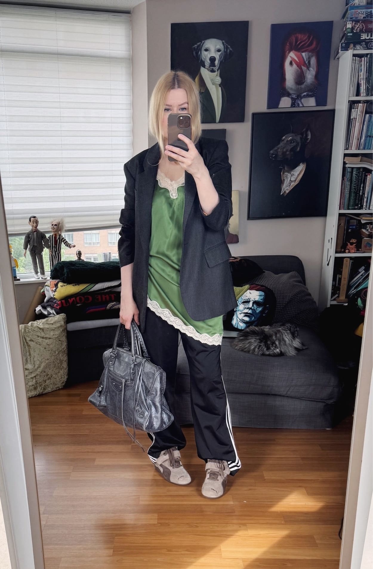 Sara of livelovesara is standing in front of a mirror taking a photo of her outfit. She is wearing a green silk slip camisole over black adidas track pants, a grey blazer, puma wedge sneakers in brown, and is carrying a grey Balenciaga city work bag.