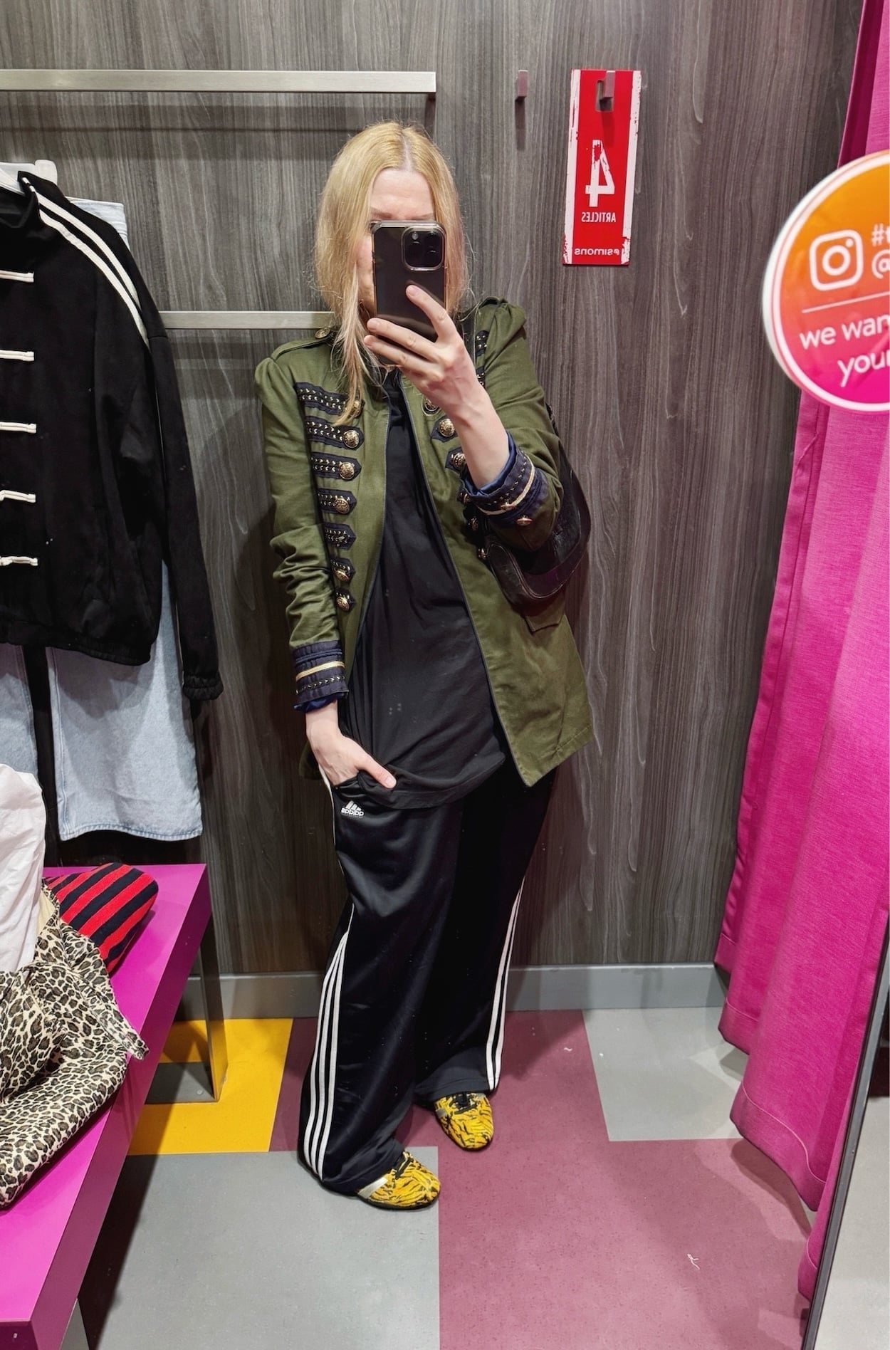 Sara of livelovesara is standing in front of a mirror taking a photo of her outfit. She is wearing an oversized black tee under a green napoleon jacket, black adidas track pants, tiger print Adidas sneakers, and is carrying a vintage Gucci Jackie bag.