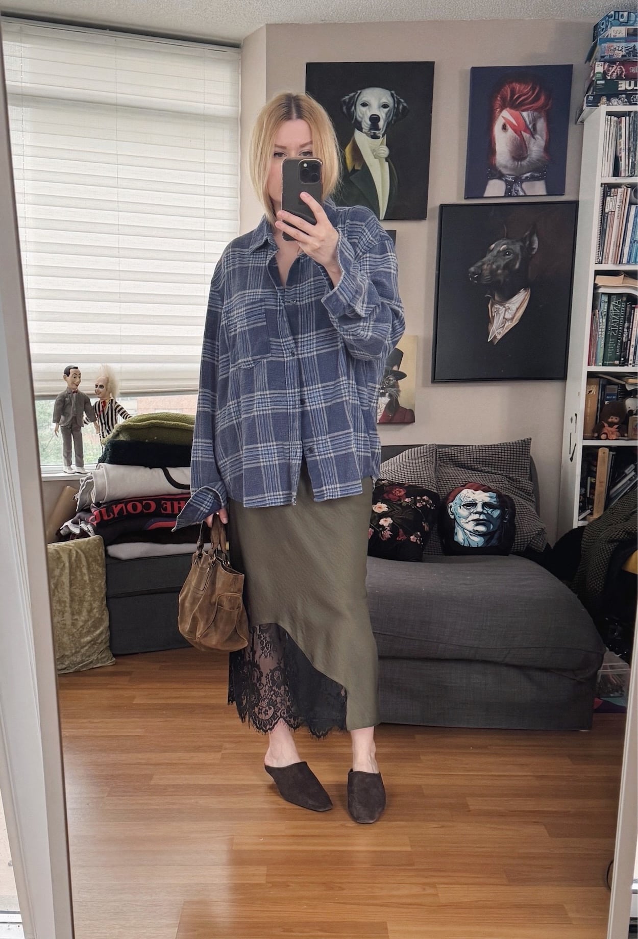 Sara of livelovesara is standing in front of a mirror taking a photo of her outfit. She is wearing an olive green slip dress under an oversized blue plaid shirt, brown suede mules, and is carrying a brown suede Celine boogie bag.