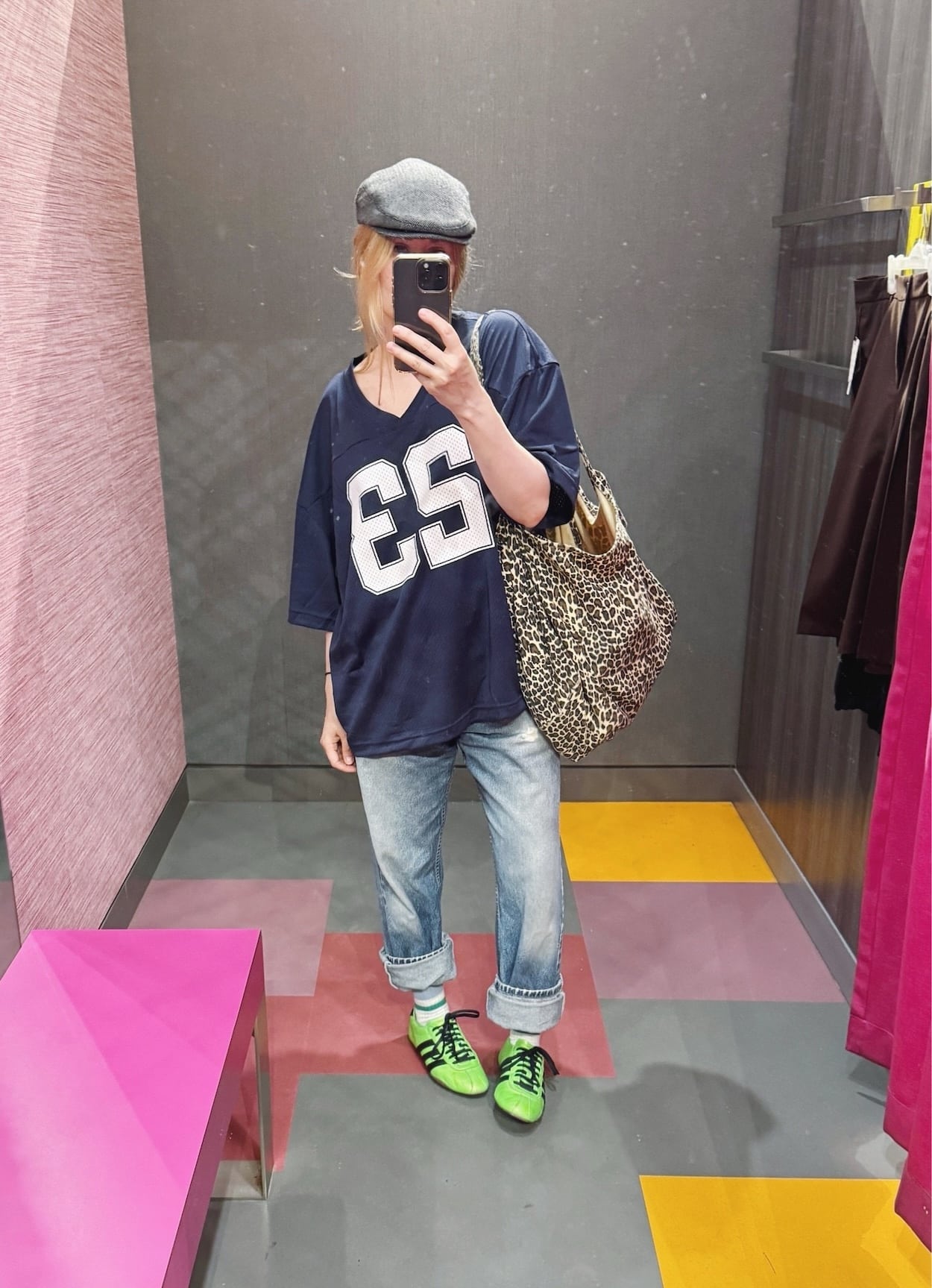Sara of livelovesara is standing in front of a mirror taking a photo of her outfit. She is wearing a navy blue football jersey paired with vintage levi's, acid green adidas sneakers, and animal print tote, and a grey driving cap.