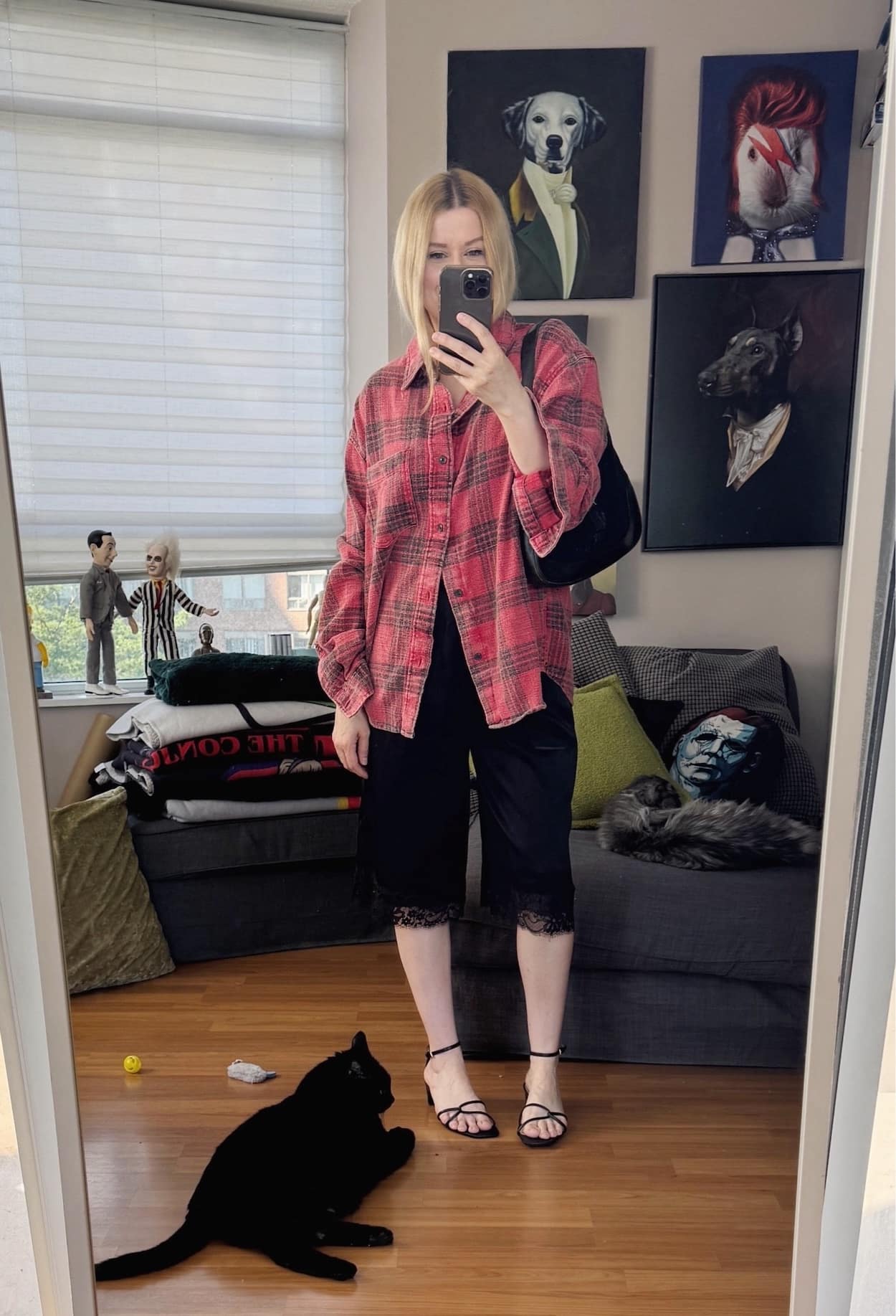 Sara of livelovesara is standing in front of a mirror taking a photo of her outfit. She is wearing a men's red plaid shirt, black silk Bermuda shorts, kitten heels and is carrying a vintage Gucci Jackie bag.