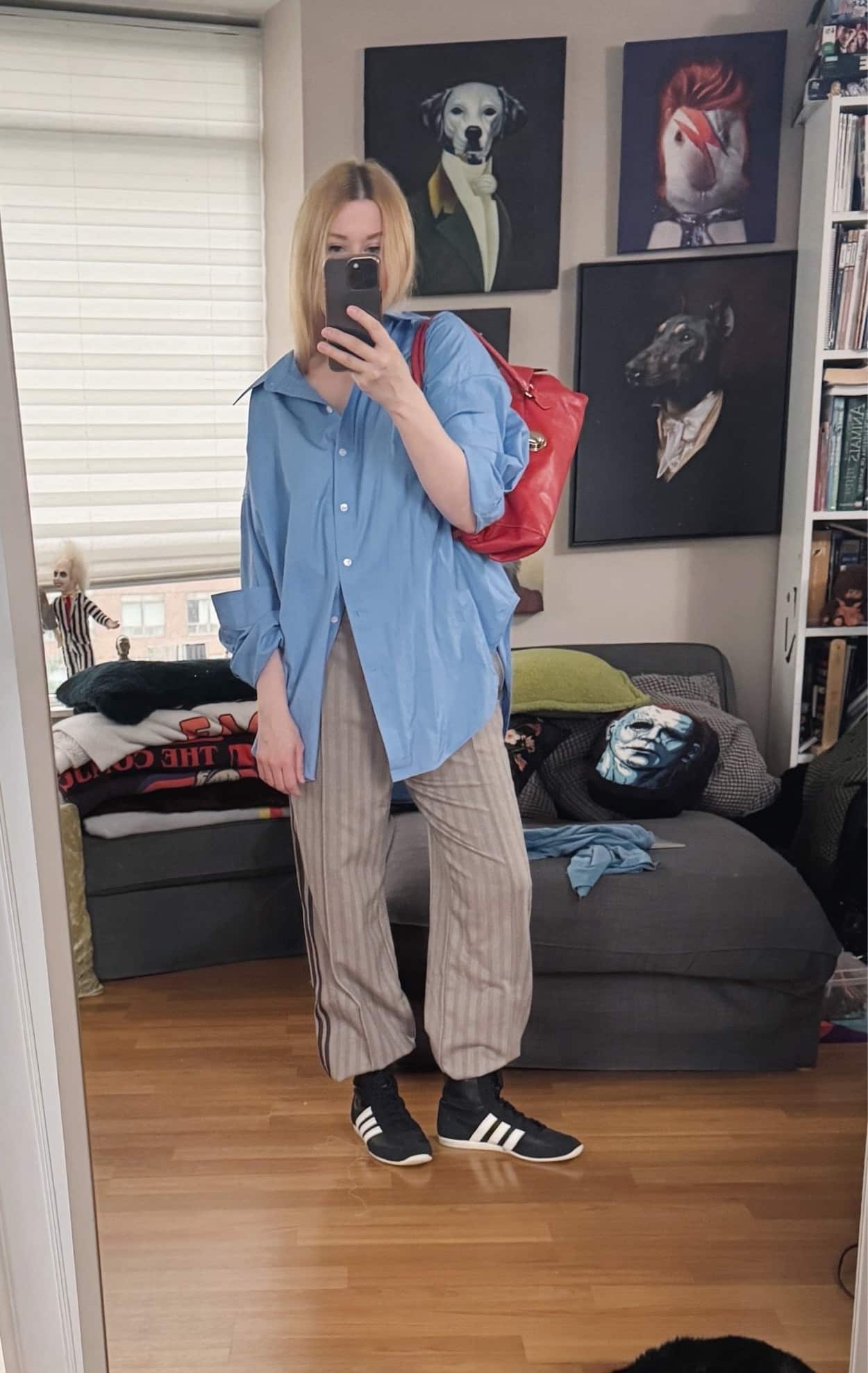Sara of livelovesara is standing in front of a mirror taking a photo of her outfit. She is wearing an oversized blue button up with houndstooth adidas track pants tucked into black Adidas wrestling boots, and is carrying a bright red Y2K Prada bag.