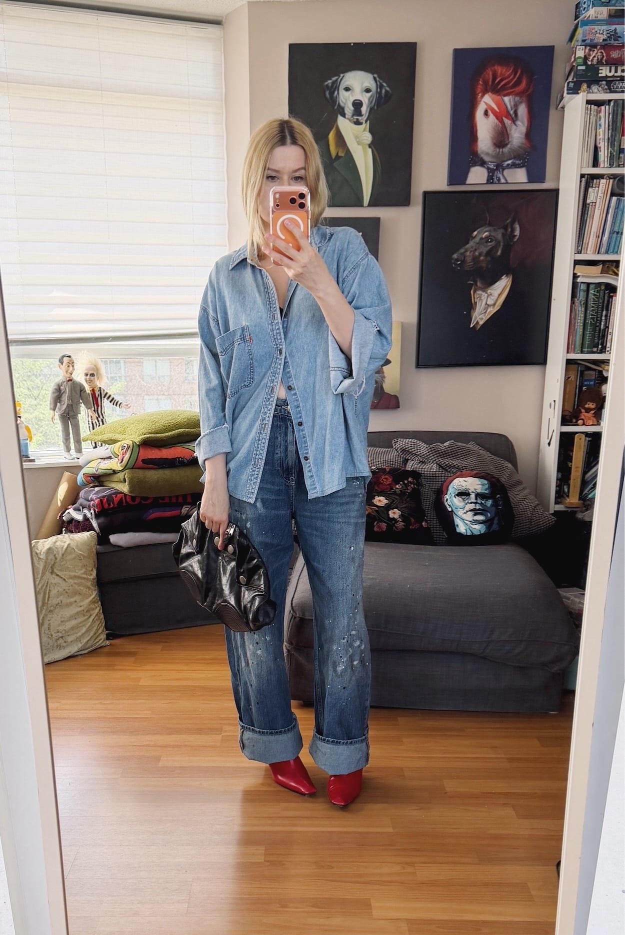 Sara of livelovesara is standing in front of a mirror taking a photo of her outfit. She is wearing a vintage levis denim shirt with pain splatter jeans, red heeled boots, and is carrying an Alexander McQueen clutch.