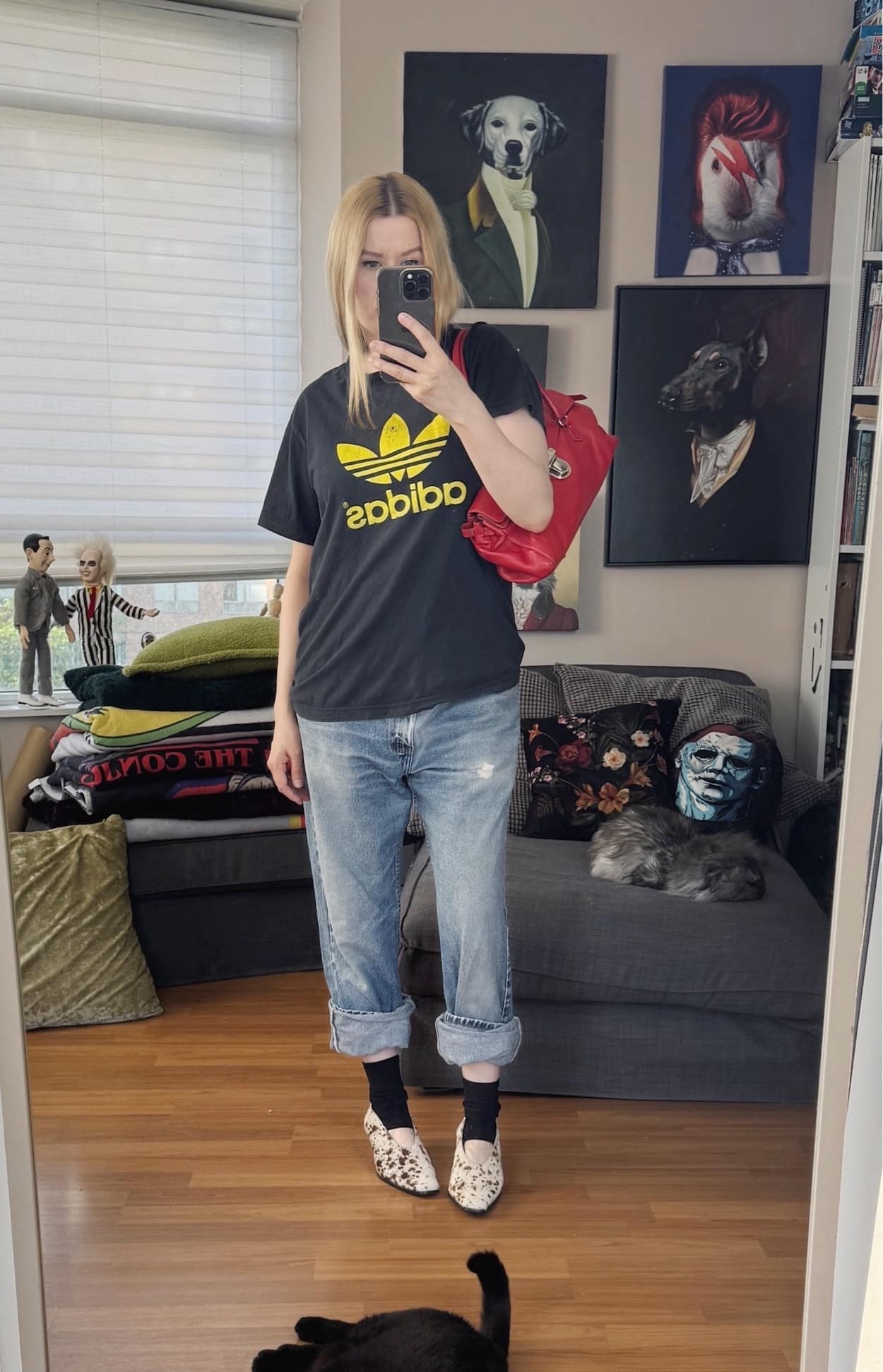 Sara of livelovesara is standing in front of a mirror taking a photo of her outfit. She is wearing a vintage Adidas t-shirt, vintage Levis, deer print heels, half socks, and is carrying a red y2k Prada bag.