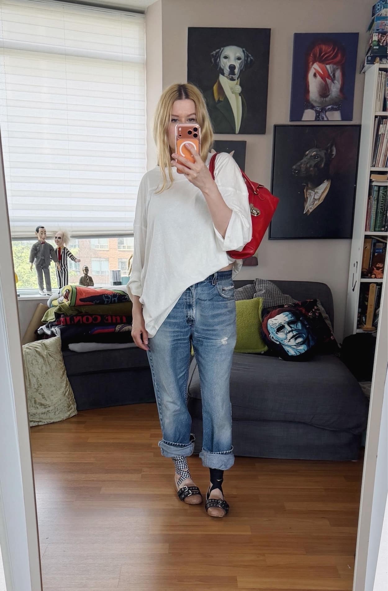 Sara of livelovesara is standing in front of a mirror taking a photo of her outfit. She is wearing an oversized white long sleeve, vintage levis, Miu Miu flats, and a red Y2K prada bag.