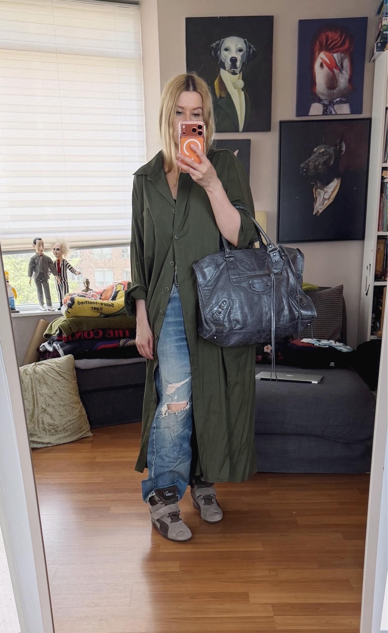 Sara of livelovesara is standing in front of a mirror taking a photo of her outfit. She is wearing an oversized green shirt dress over distressed vintage levis, Puma Wedge sneakers, and is carrying a large Balenciaga work bag in grey.
