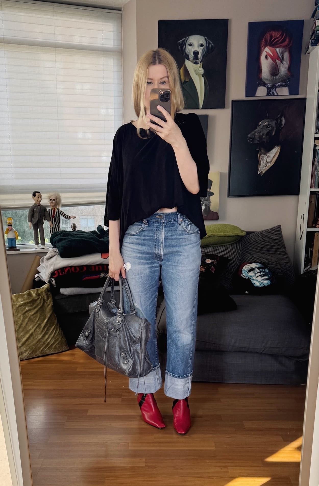Sara of livelovesara is standing in front of a mirror taking a photo of her outfit. She is wearing an oversized men's black t-shirt, vintage levis 517s, red boots, and a grey Balenciaga city work bag.