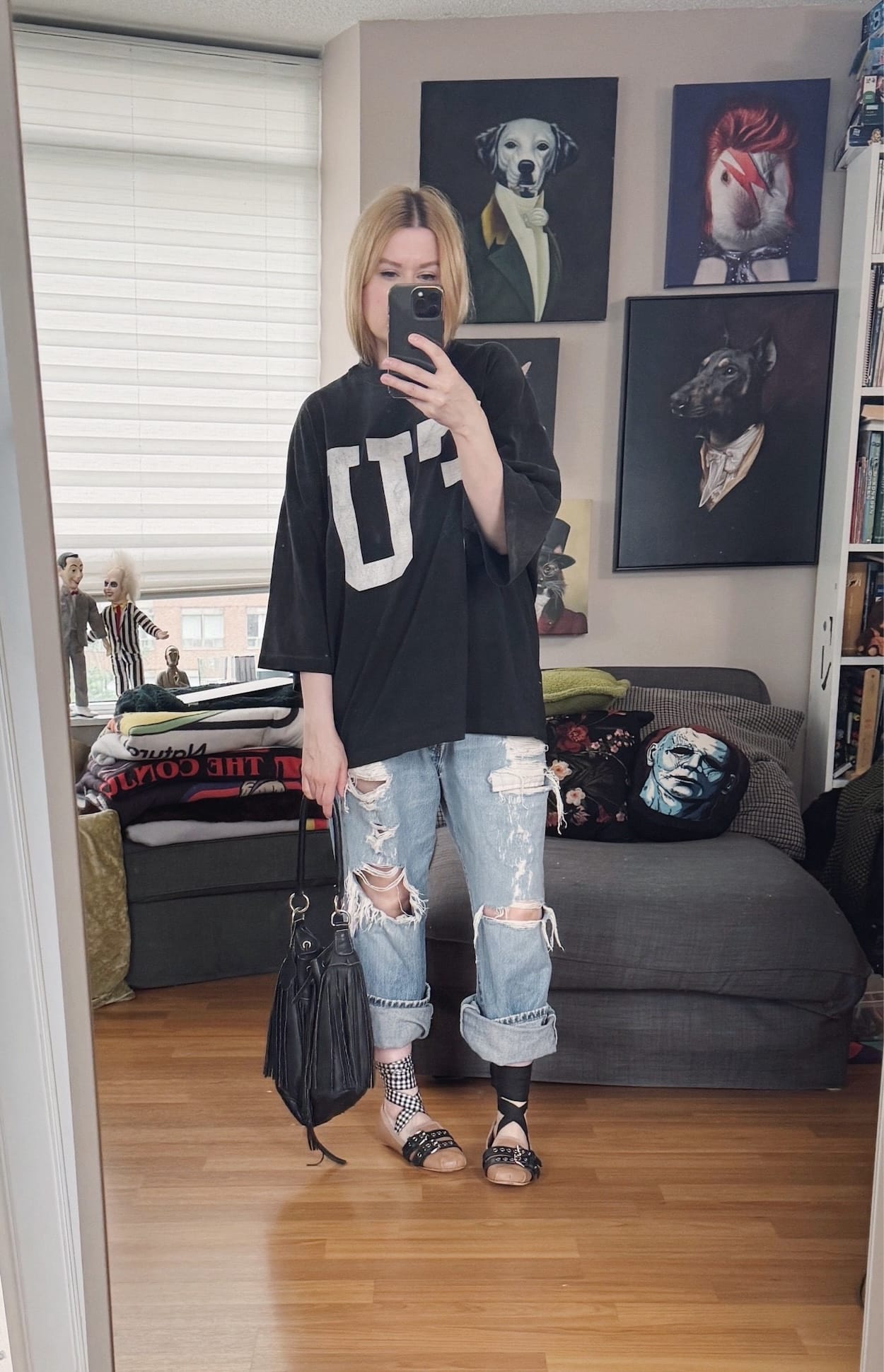 Sara of livelovesara is standing in front of a mirror taking a photo of her outfit. She is wearing an oversized FU t-shirt with distressed vintage levis that are rolled up over pink Miu Miu ballet flats with ribbons at the ankles. She is carrying a black leather fringe bucket bag,