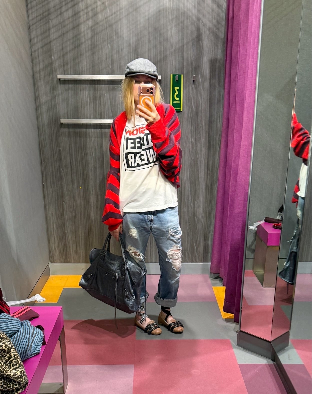 Sara of livelovesara is standing in front of a mirror taking a photo of her outfit. She is wearing a Vision Streetwear t-shirt under a striped sweater worn as a shrug, vintage Levis, Miu Miu flats, a grey herringbone flat cap, and is carrying a large, grey Balenciaga work bag.