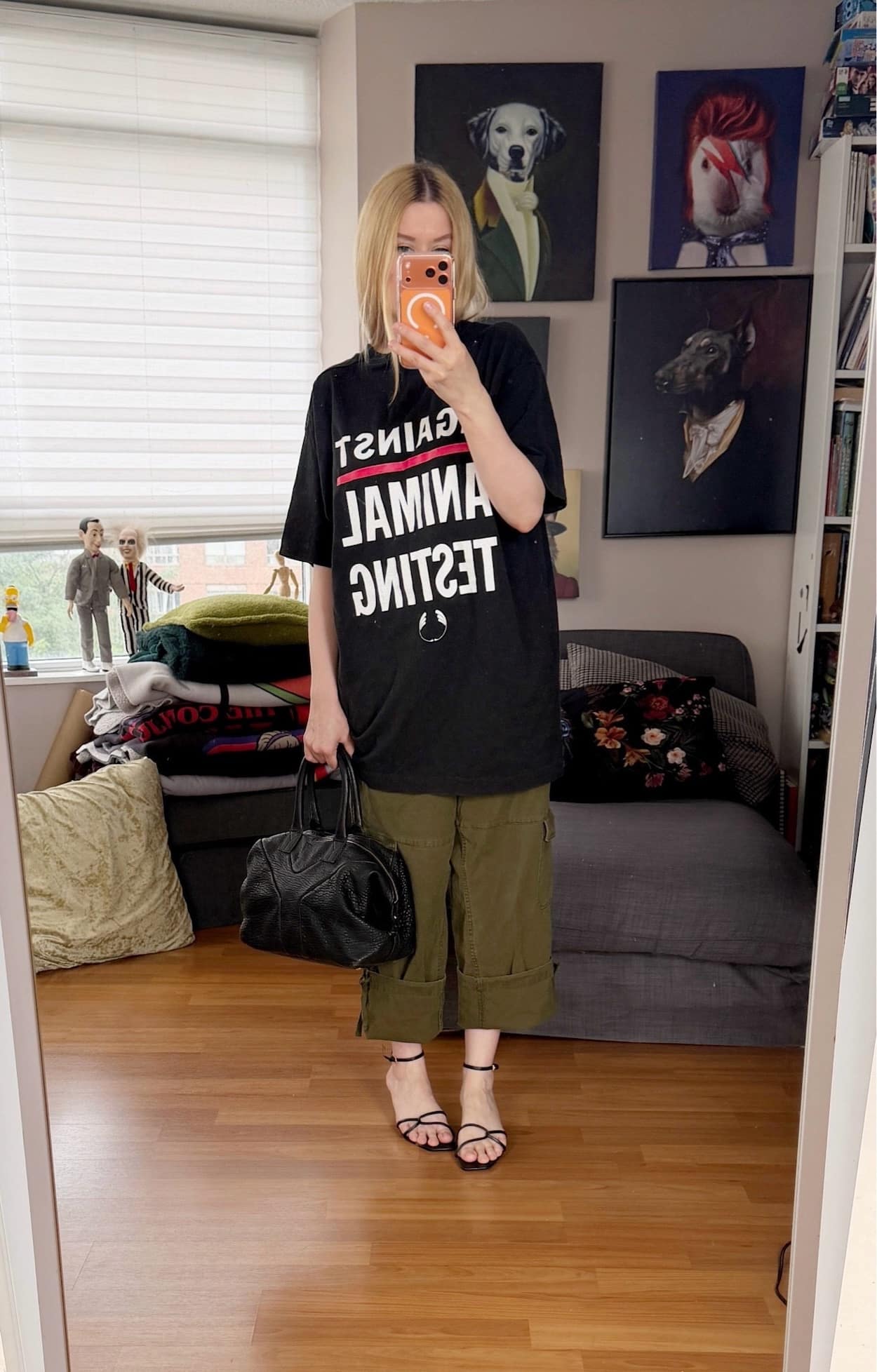 Sara of livelovesara is standing in front of a mirror taking a photo of her outfit. She is wearing an Against Animal Testing Body Shop t-shirt with cuffed cargos, strappy sandals, and a black YSL easy bag.