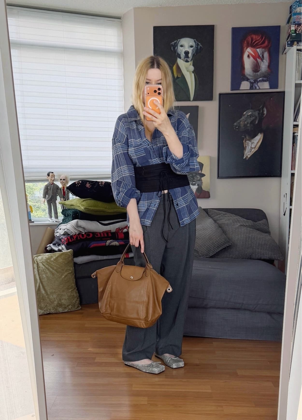 Sara of livelovesara is standing in front of a mirror taking a photo of her outfit. She is wearing a blue plaid shirt with a black cummerbund over it, grey relaxed trousers, snake print mules, and is carrying a brown leather Longchamp le pliage bag