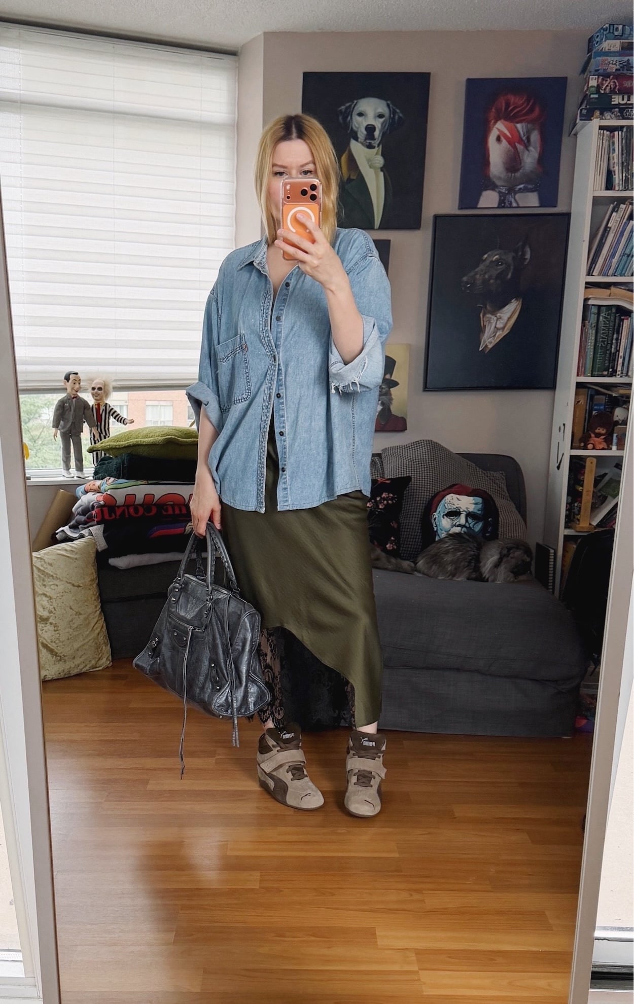 Sara of livelovesara is standing in front of a mirror taking a photo of her outfit. She is wearing a vintage levis denim shirt over a green slip dress, Puma Wedge sneakers, and a large, grey Balenciaga work bag.
