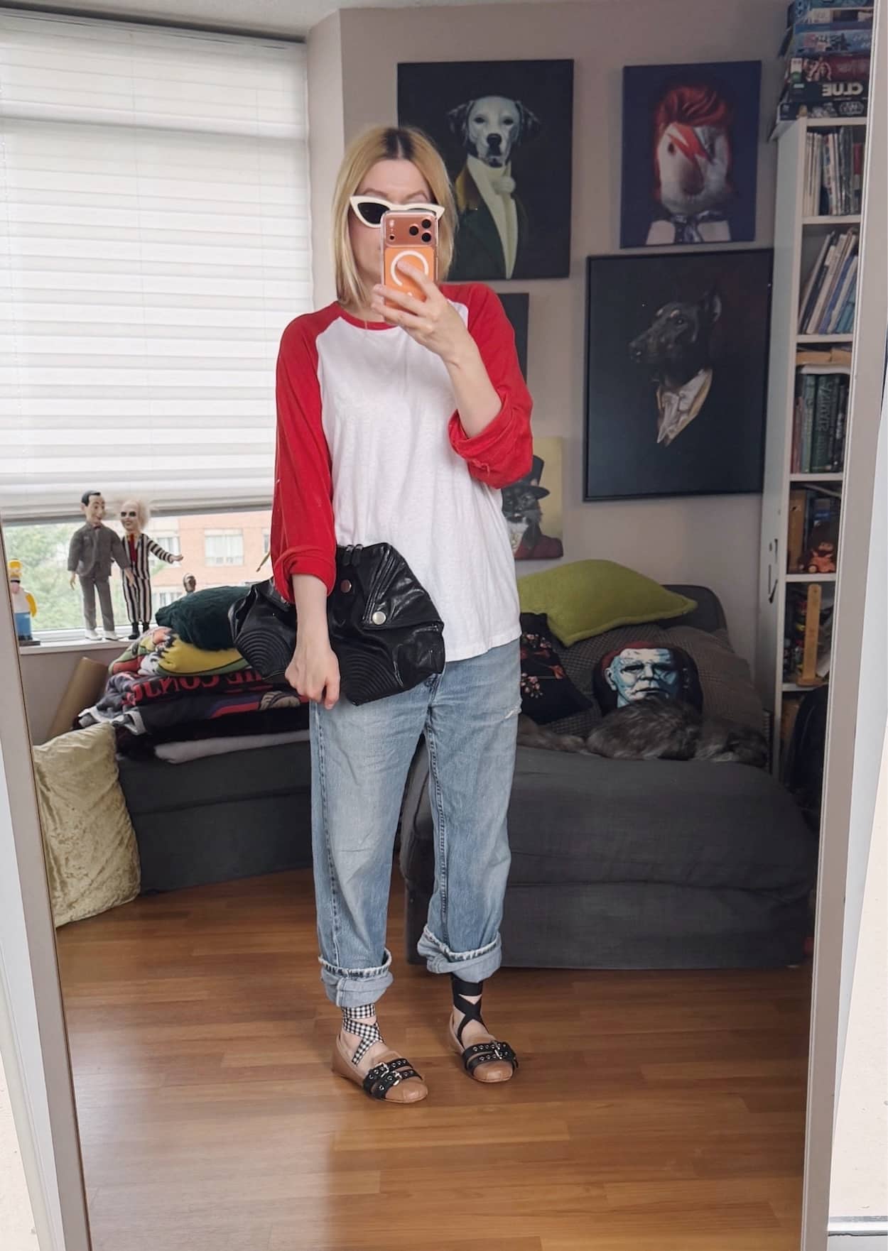 Sara of livelovesara is standing in front of a mirror taking a photo of her outfit. She is wearing an oversized red and white baseball shirt with vintage Levi's, Miu Miu flats, off-white Celine cat eye sunglasses, and an Alexander McQueen clutch.
