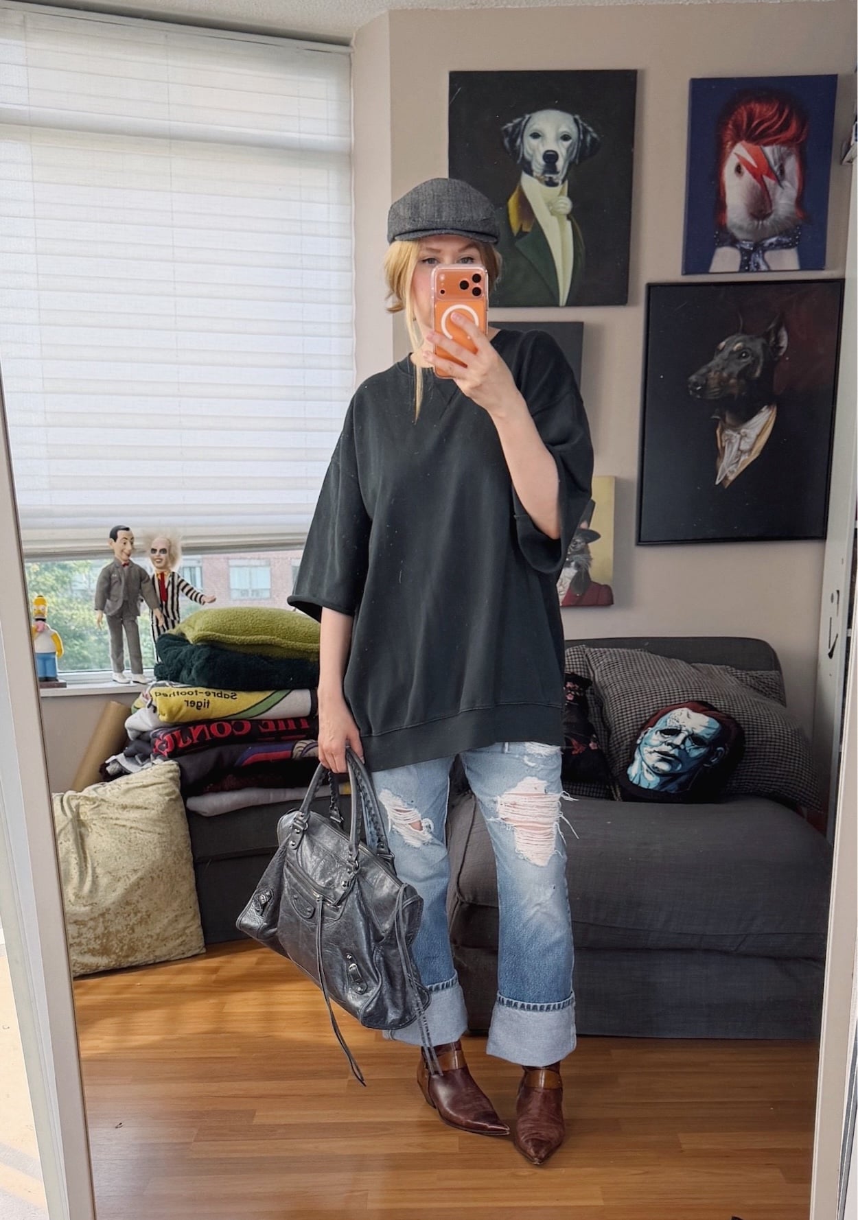 Sara of livelovesara is standing in front of a mirror taking a photo of her outfit. She is wearing an oversized dark grey short sleeve sweatshirt with vintage Levis, brown pointy toe 90s boots, a grey herringbone flat cap, and is carrying a large Balenciaga city work bag.