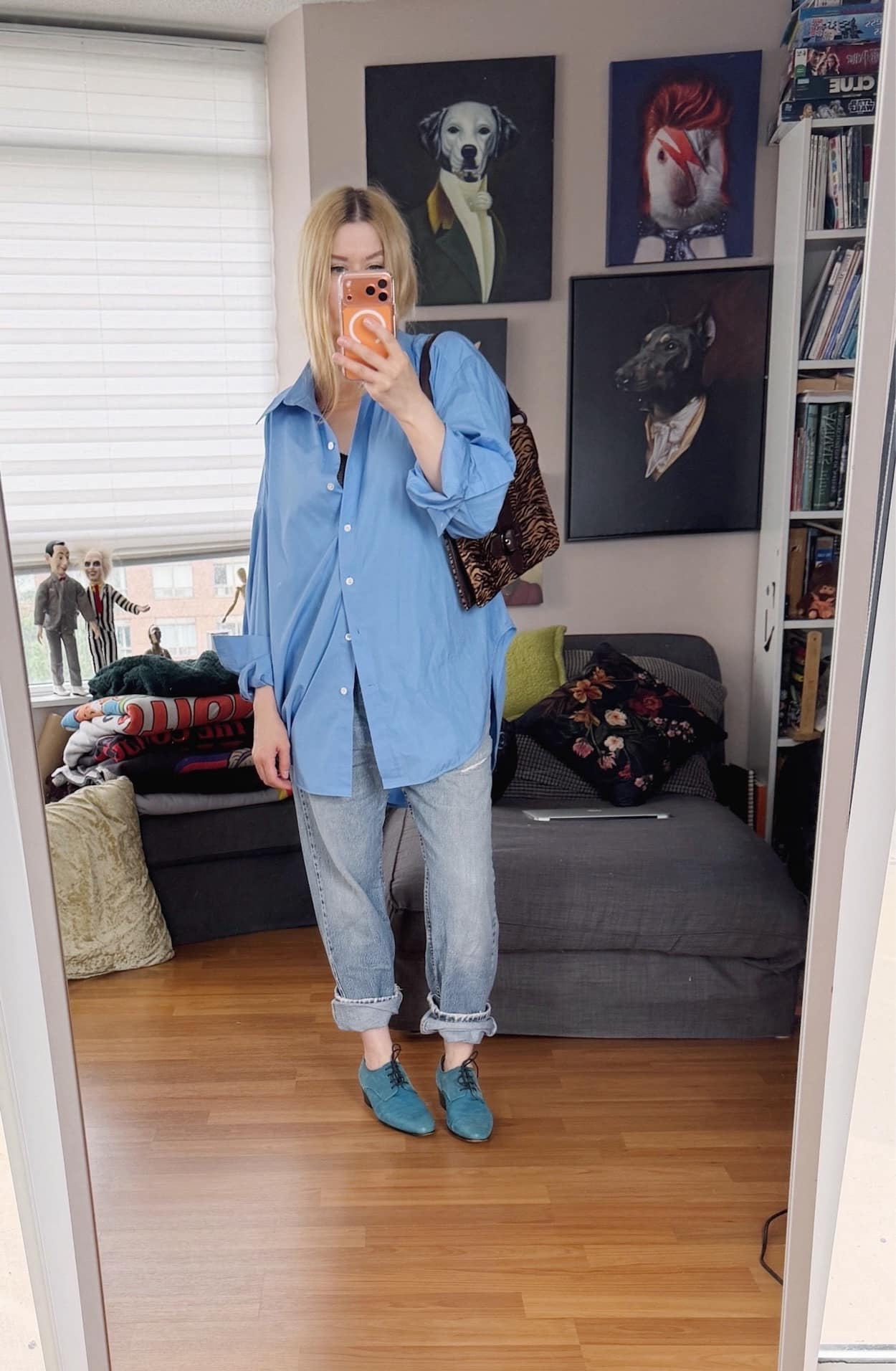 Sara of livelovesara is standing in front of a mirror taking a photo of her outfit. She is wearing an oversized blue button up with cuffed vitnage Levis, blue brogues, and a vintage tiger print bag.
