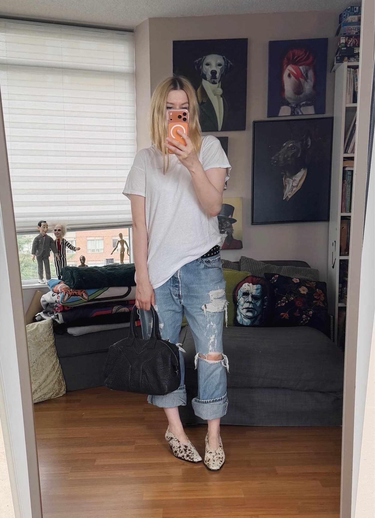 Sara of livelovesara is standing in front of a mirror taking a photo of her outfit. She is wearing an white Hanes tee with distressed vintage Levi's deer print heels, and is carrying a YSL easy bag.