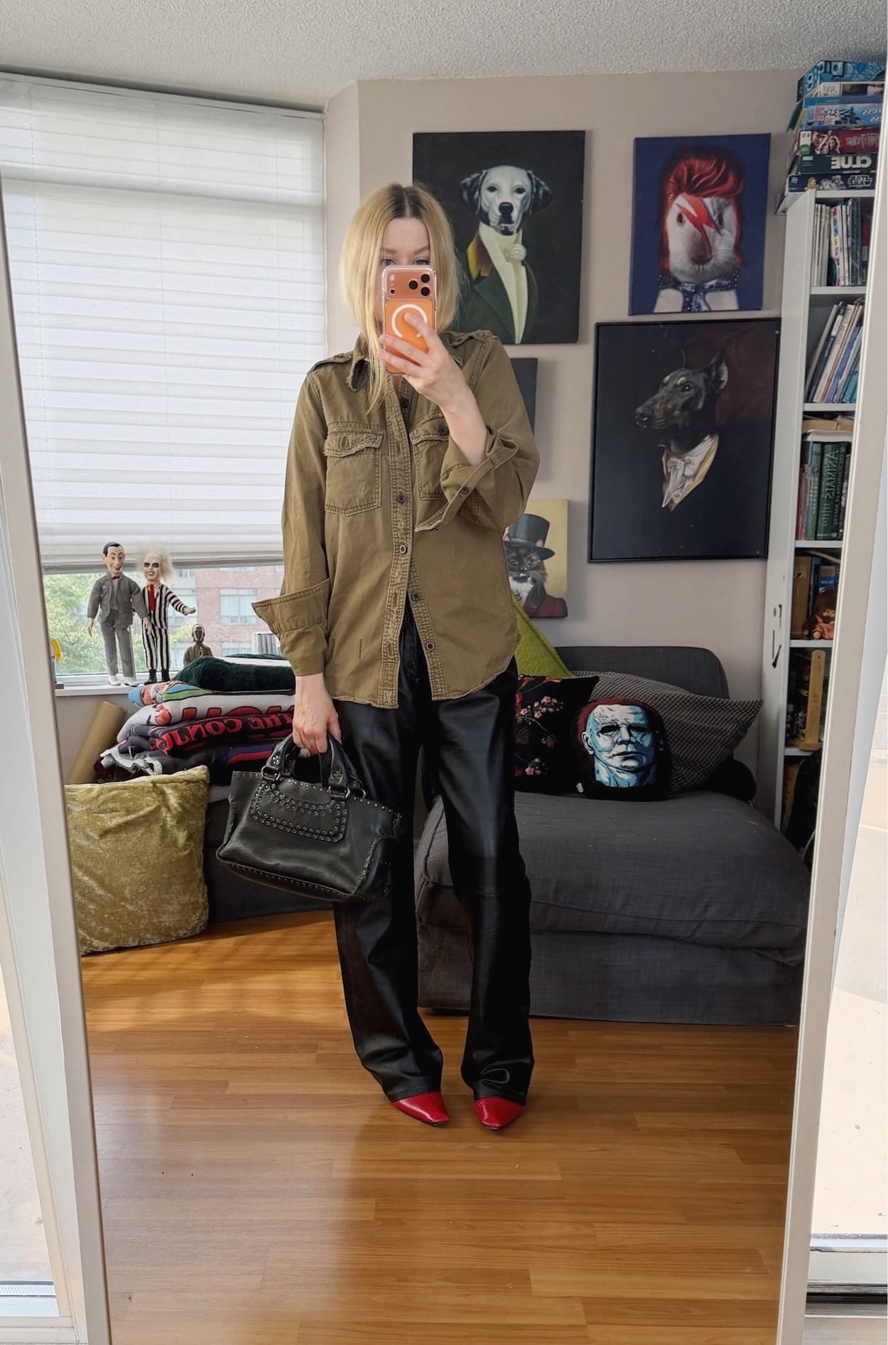 Sara of livelovesara is standing in front of a mirror taking a photo of her outfit. She is wearing a y2k era miltary shirt, with vintage DKNY leather pants, red vintage boots, and is carrying a Celine Boogie Bag.