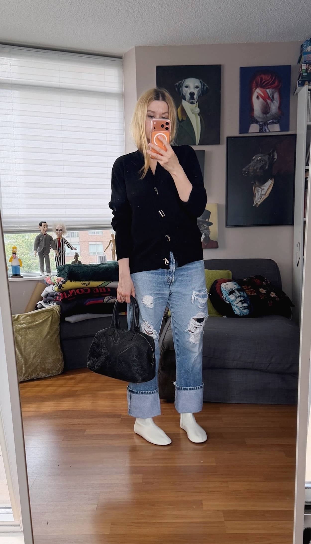 Sara of livelovesara is standing in front of a mirror taking a photo of her outfit. She is wearing a black cardigan with buttons that spell fuck, vintage Levis, cream sock boots, and is carrying a YSL easy bag in black leather.