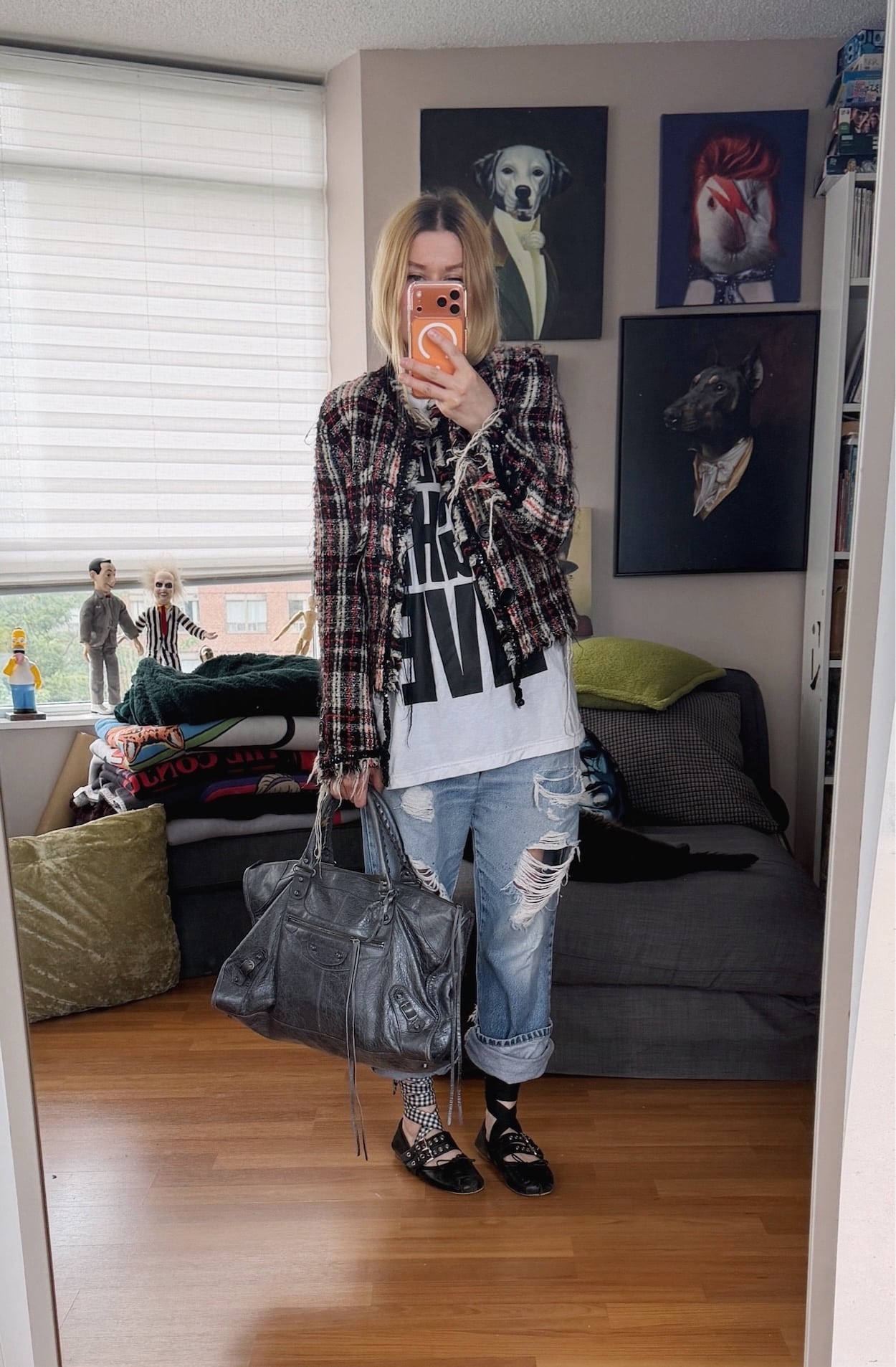 Sara of livelovesara is standing in front of a mirror taking a photo of her outfit. She is wearing a white t-shirt with Saturday Night Live in large black letters under a plaid tweed acket, vintage levis cuffed over tie ankle Miu Miu ballet flats, and is carrying a Balenciaga work bag.