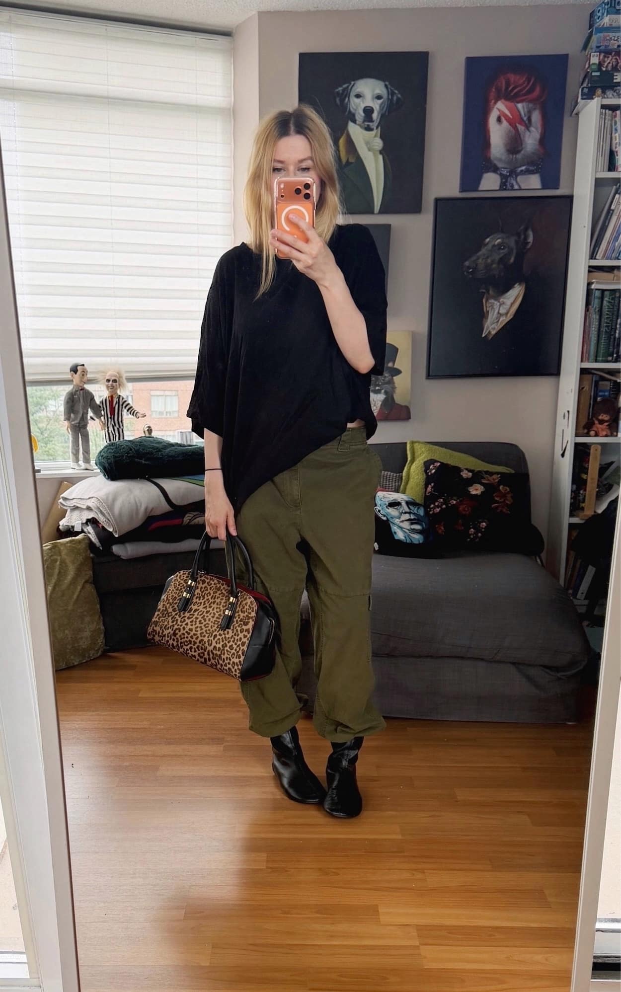 Sara of livelovesara is standing in front of a mirror taking a photo of her outfit. She is wearing an oversized black t-shirt with relaxed green cargo pants tucked into black flat boots, and is carrying an animal print Ferragamo bag.