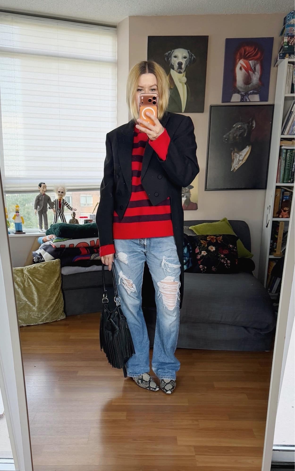 Sara of livelovesara is standing in front of a mirror taking a photo of her outfit. She is wearing a red and brown striped sweater under a vintage tailcoat, vintage distressed levis, snake print flat boots, and is carrying a vintage fringe leather bucket bag.
