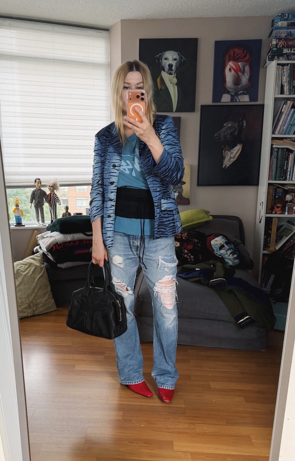 Sara of livelovesara is standing in front of a mirror taking a photo of her outfit. She is wearing a blue vintage Stussy t-shirt with a black cummerbund. A blue tiger print Moschino blazer, vintage Levis, red boots, and a YSL Easy bag.