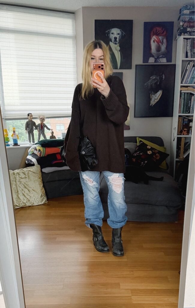 Sara of livelovesara is standing in front of a mirror taking a photo of her outfit. She is wearing an oversized brown sweater with distressed vintage levis tucked into frye engineer boots, and is carrying an Alexander McQueen de manta clutch.