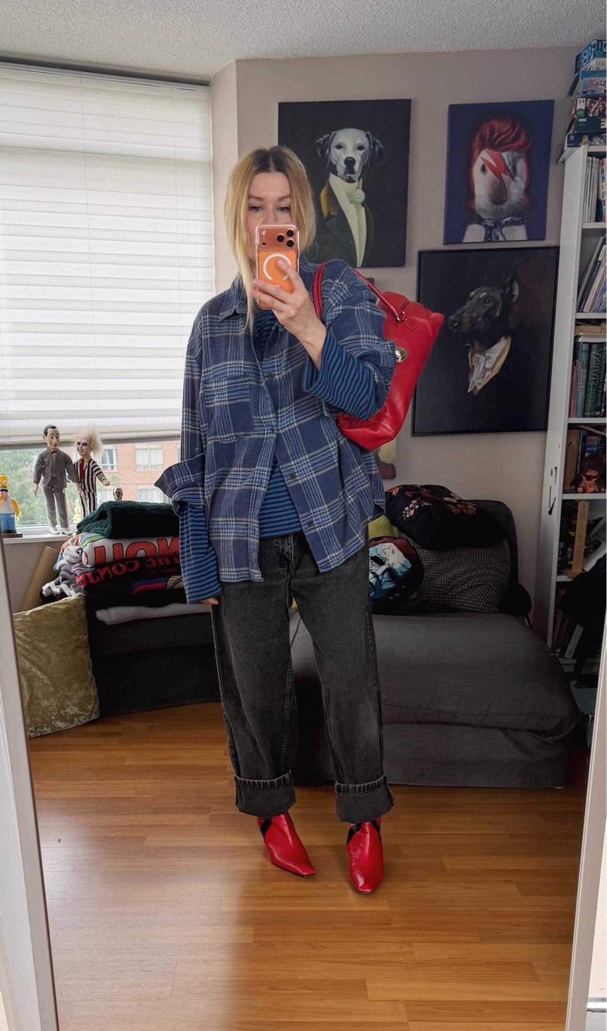 Sara of livelovesara is standing in front of a mirror taking a photo of her outfit. She is wearing a blue striped shirt under a blue plaid shirt with worn black vintage Levis, red boots, and a red prada bag.