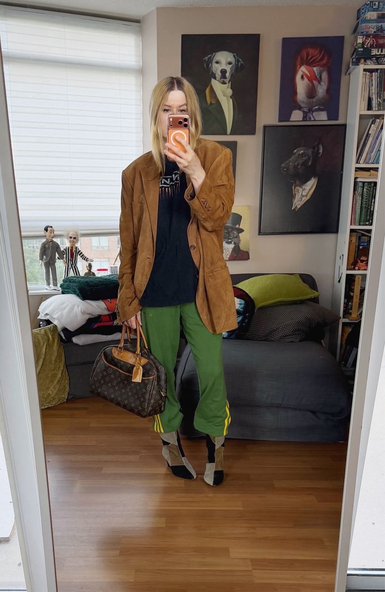 Sara of livelovesara is standing in front of a mirror taking a photo of her outfit. She is wearing a Nine Inch nails t-shirt under an oversized brown suede blazer, green Adidas track pants, Isabel Marant patch boots, and is carrying a Louis Vuitton bag.