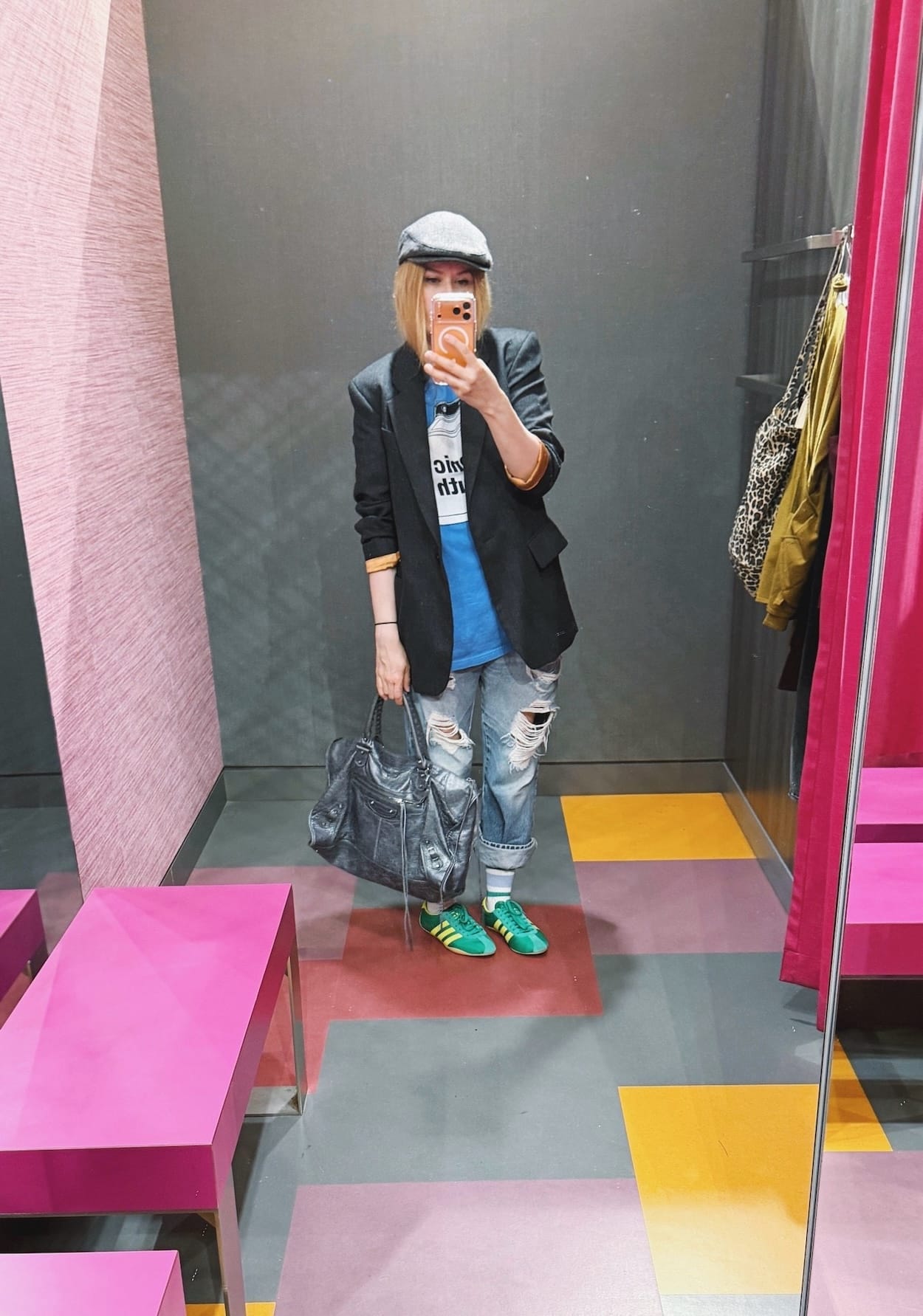 Sara of livelovesara is standing in front of a mirror taking a photo of her outfit. She is wearing a blue Sonic Youth Washing Machine t-shirt under a grey Vivienne Westwood blazer, vintage Distressed Levis cuffed over striped sports socks, Green and yellow Adidas Tokyo sneakers, a grey flat cap, and grey Balenciaga work bag.