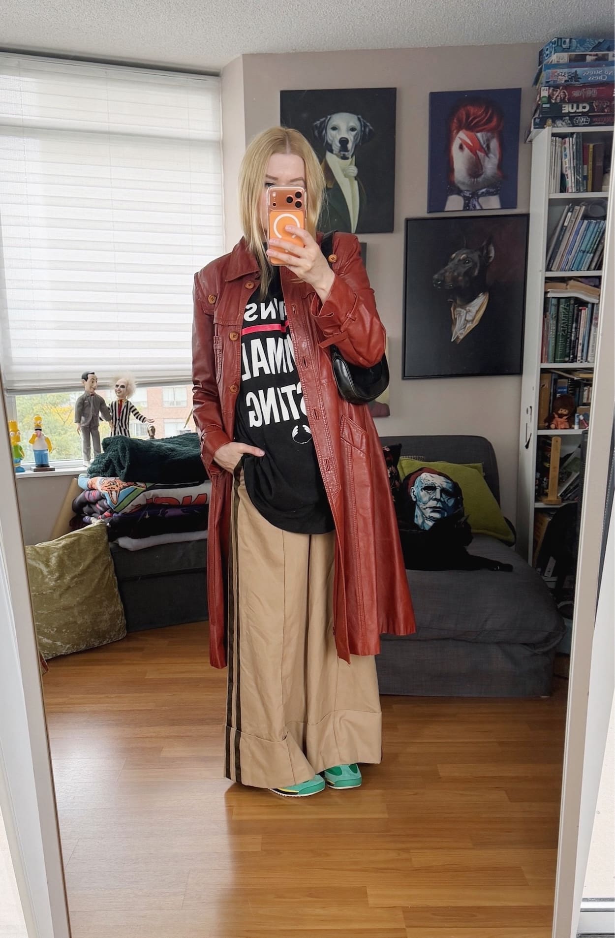 Sara of livelovesara is standing in front of a mirror taking a photo of her outfit. She is wearing a vintage The Body Shop Against Animal Testing t-shirt with wide leg tan trousers, a burgundy vintage leather trench, green Adidas, and is carrying a vintage Gucci Jackie bag.