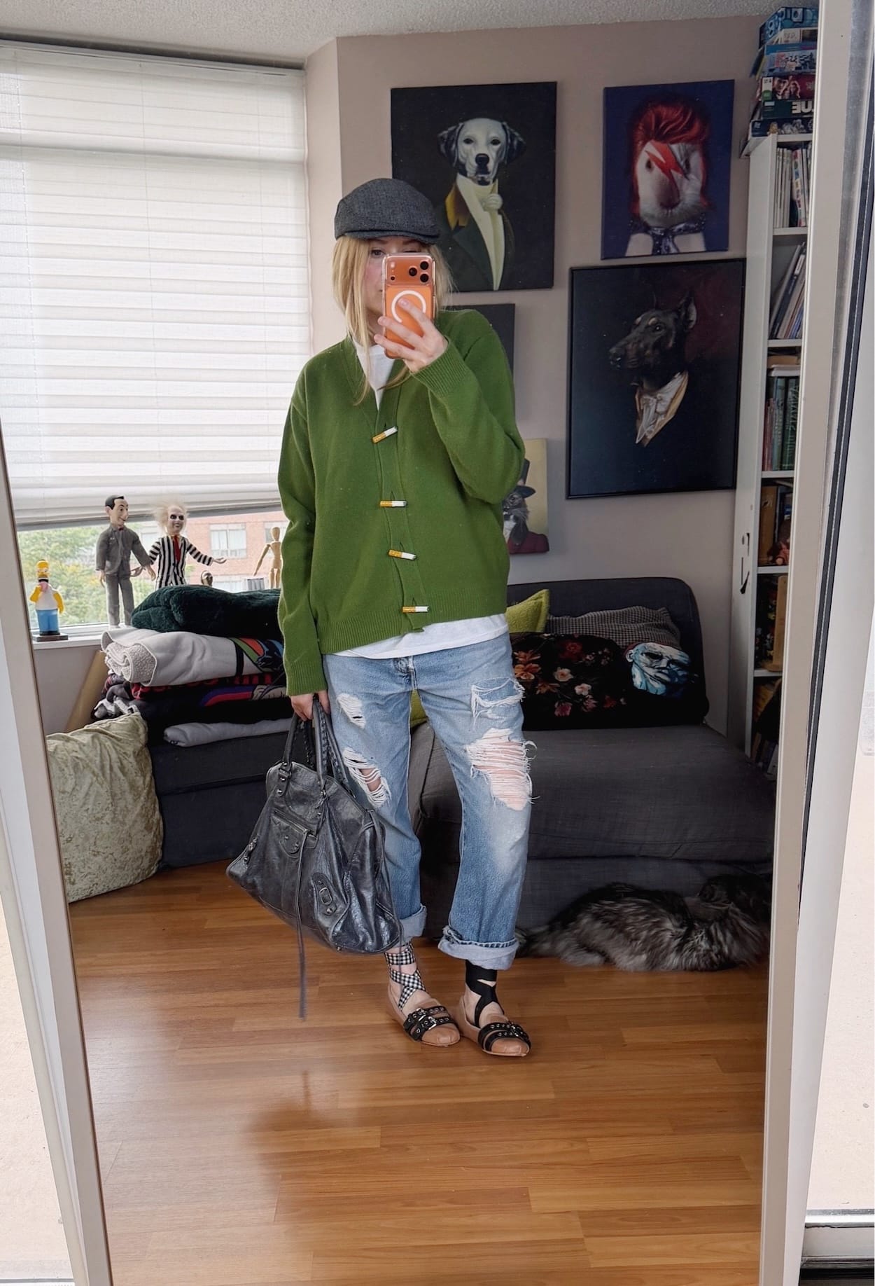 Sara of livelovesara is standing in front of a mirror taking a photo of her outfit. She is wearing a Green Hades Wool Cigarette Button Cardigan, over a white tee, vintage levis, Miu Miu flats, a flat cap, and a large grey Balenciaga work bag.